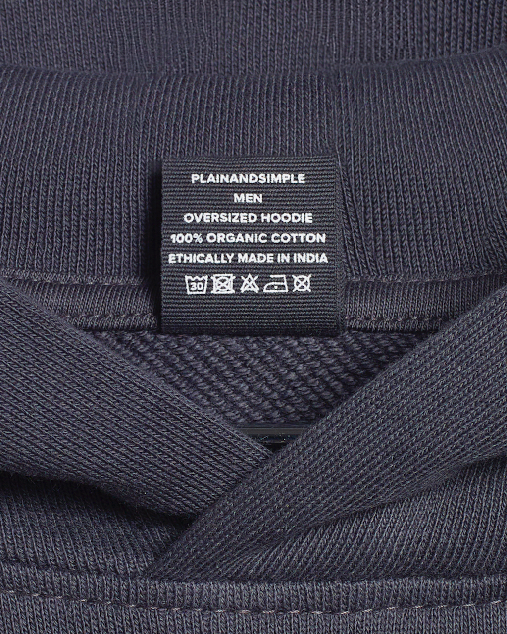 A close up of the neck label in a dark grey, oversized, organic cotton hoodie.