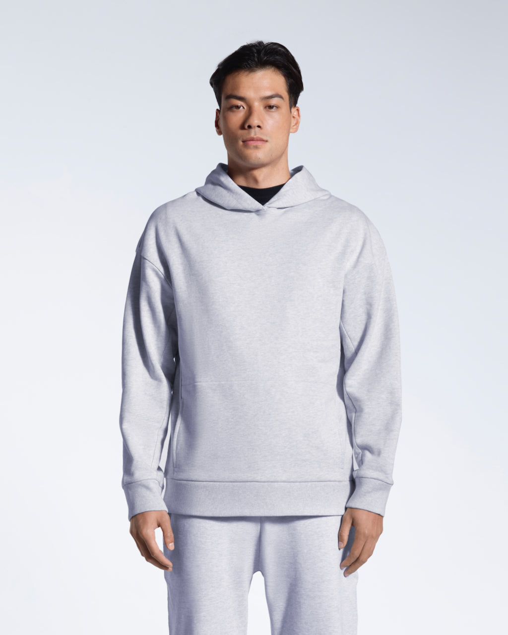 A man looking into the camera with his arms by his sides, modelling a grey oversized organic cotton hoodie with matching joggers.