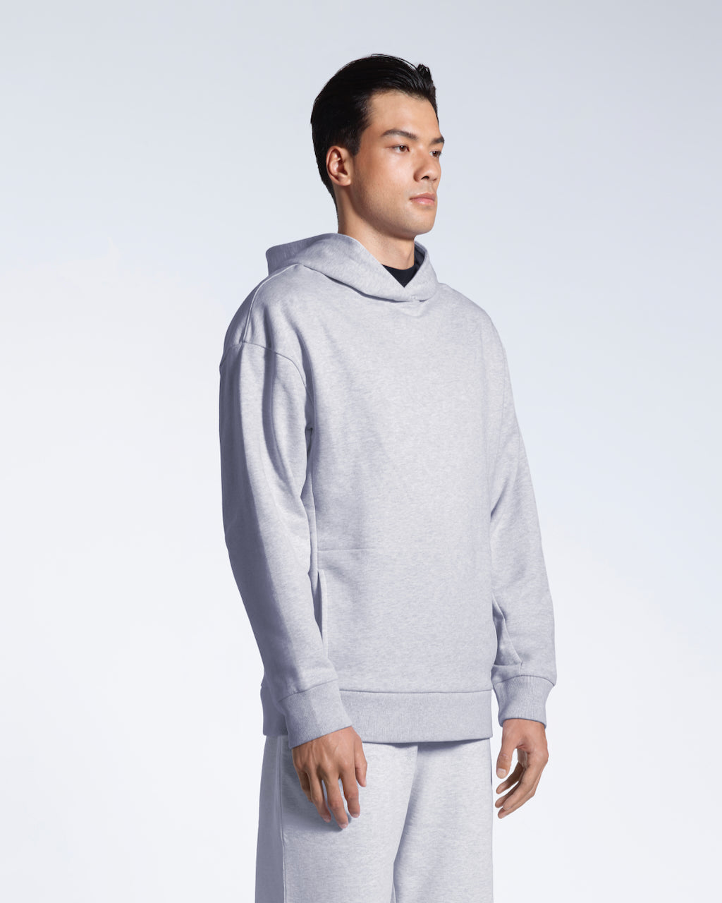 A man at an angle looking away from the camera with his arms by his side, modelling a grey oversized organic cotton hoodie with matching joggers.