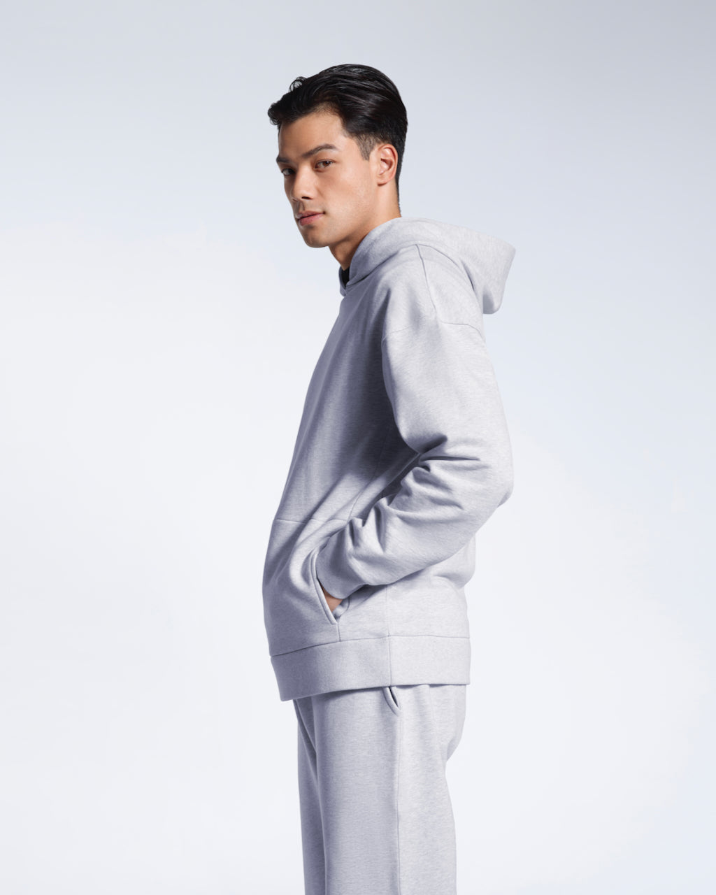 A man facing side on looking into the camera, modelling a grey oversized organic cotton hoodie with matching joggers.