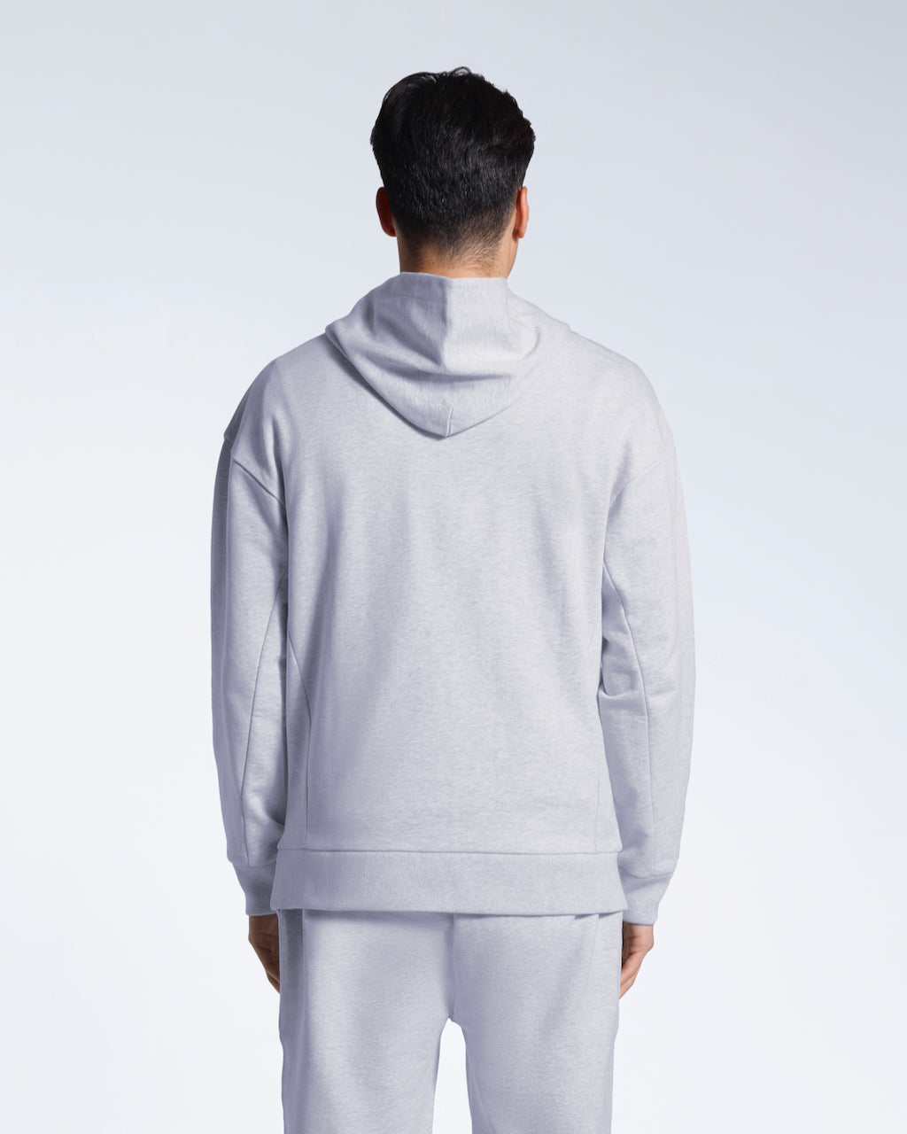 A man facing away from the camera with his arms by his sides, modelling a grey oversized organic cotton hoodie with matching joggers.