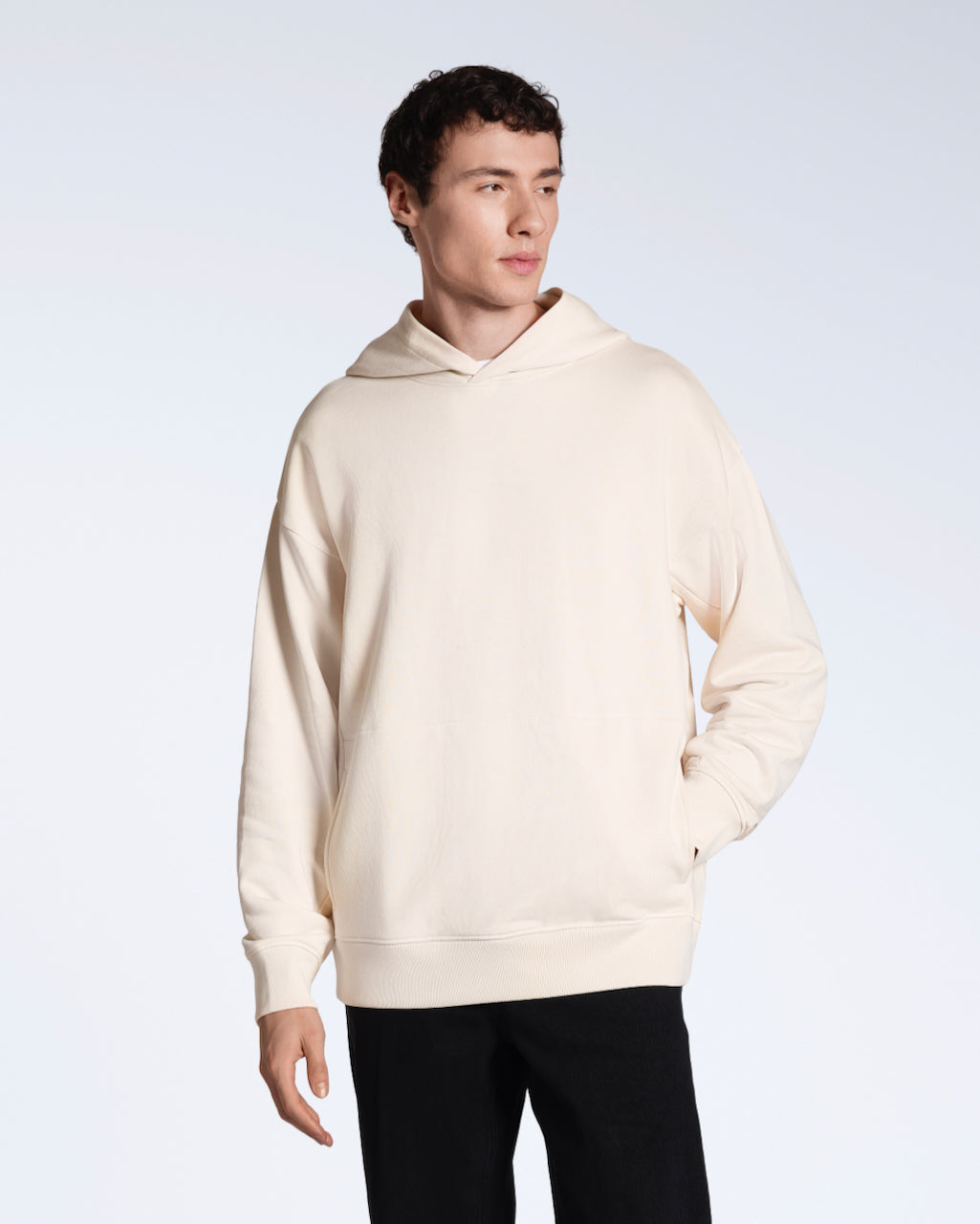 A man looking away from the camera with a hand in his pocket, modelling a natural coloured oversized organic cotton hoodie.