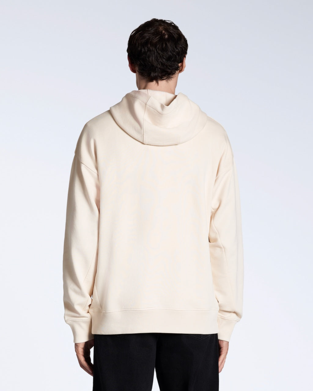 A man facing away from the camera with his arms by his sides, modelling a natural coloured oversized organic cotton hoodie.