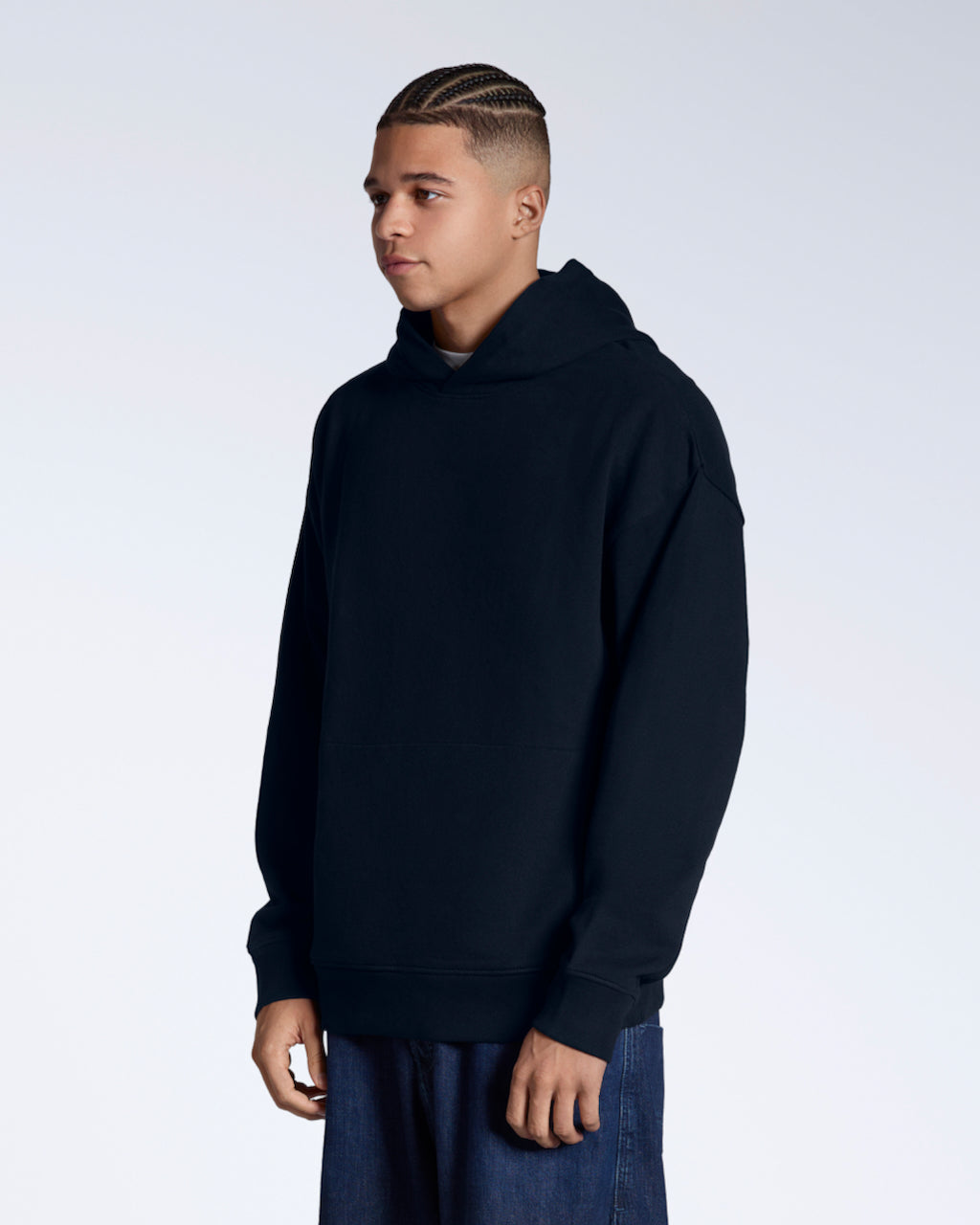 A man at an angle looking away from the camera with his arms by his side, modelling a nnavy oversized organic cotton hoodie.