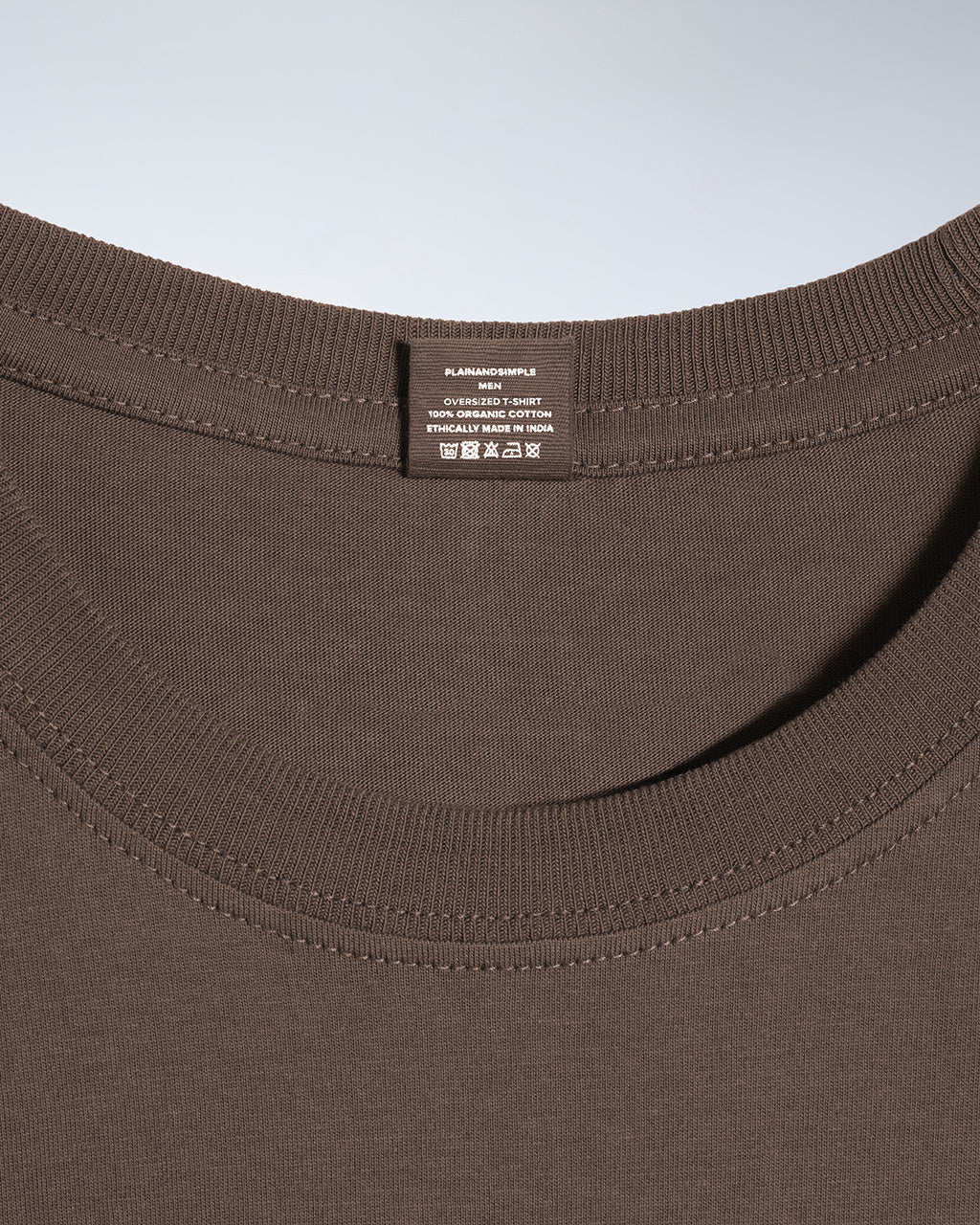 A close up of a neck label in a men's dark khaki, oversized, organic cotton t shirt.