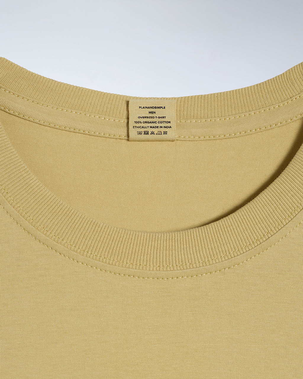 A close up of a neck label in a men's light khaki, oversized, organic cotton t shirt.
