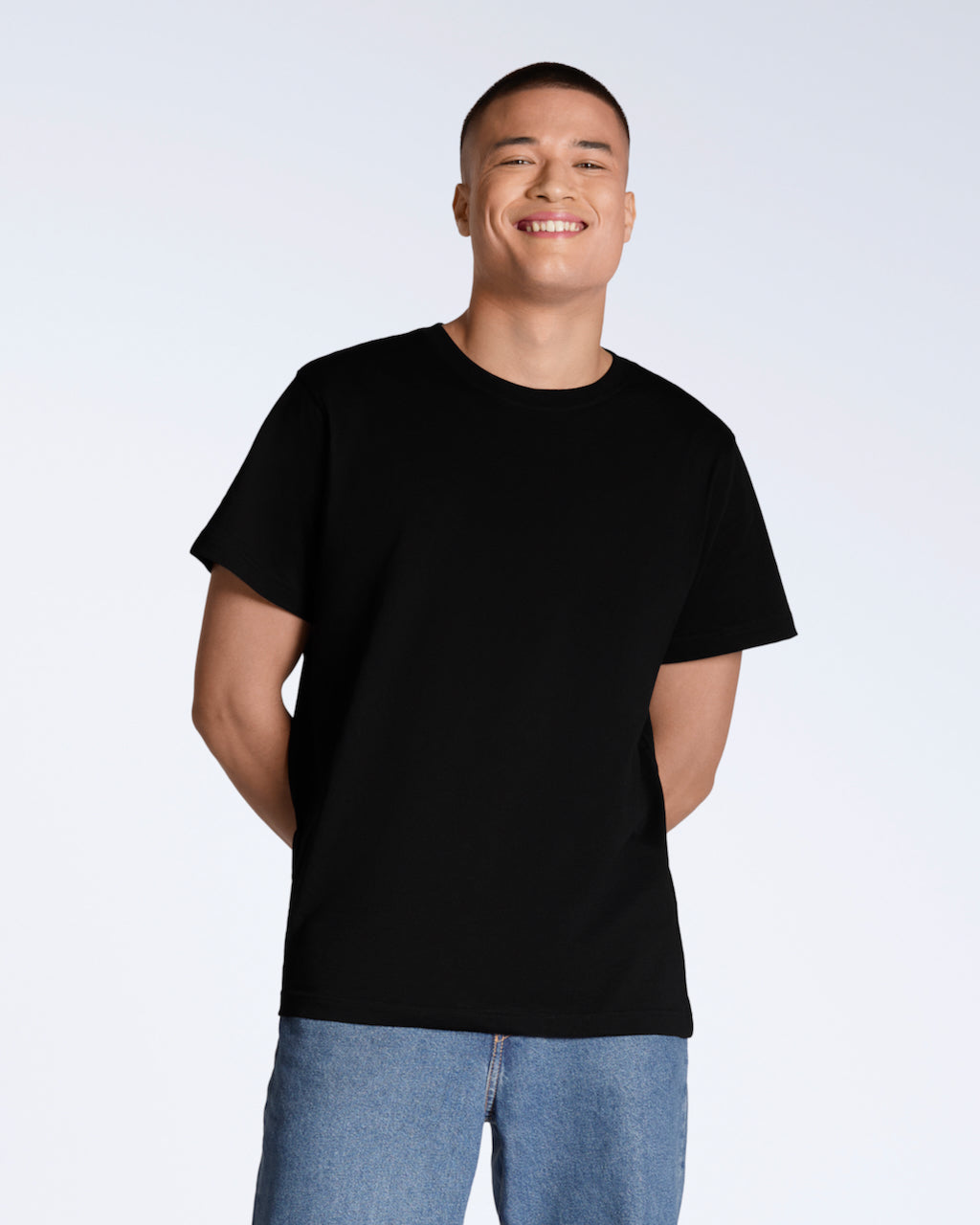 A man smiling into the camera with his hands behind his back, modelling a plain black, organic cotton t shirt.