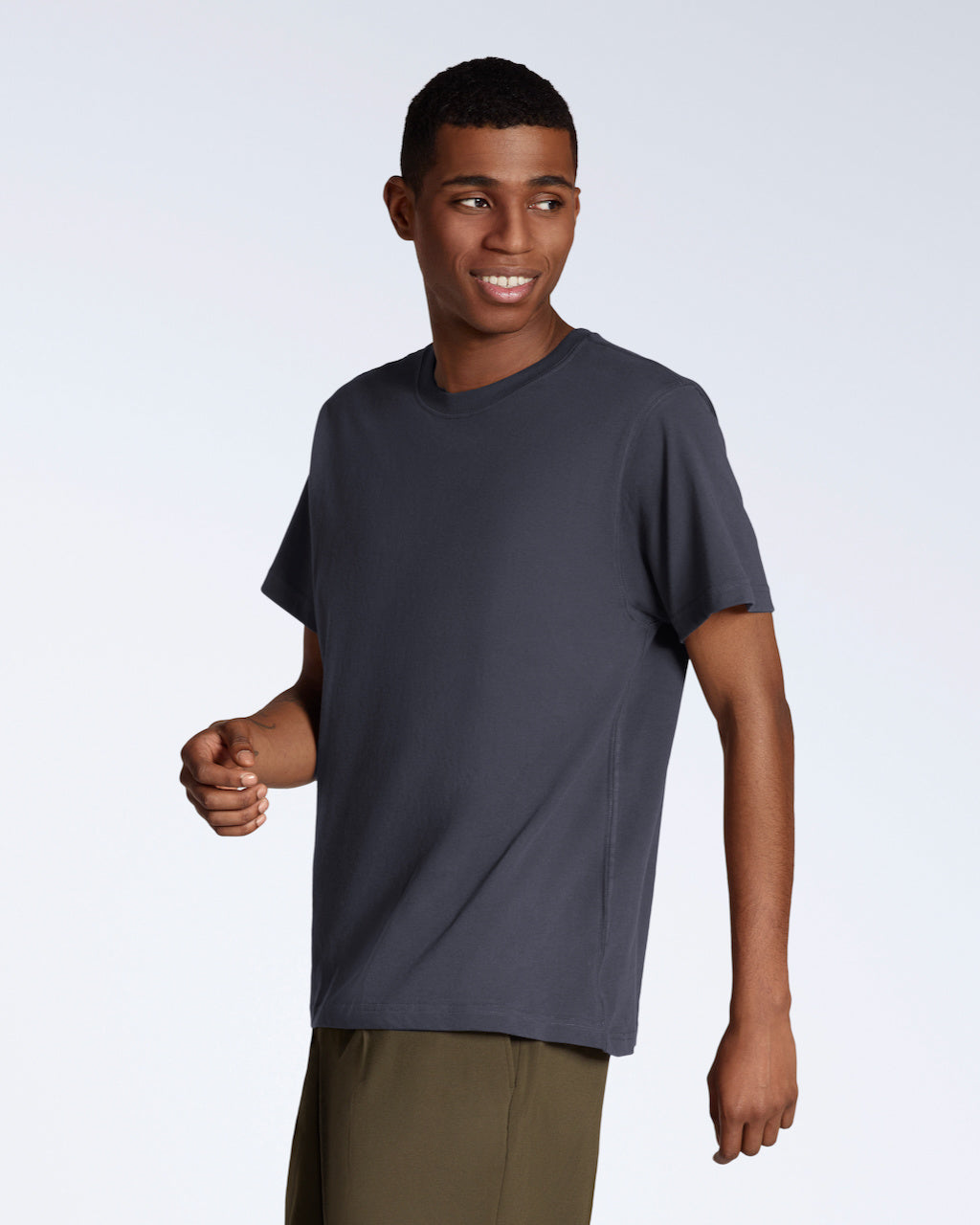 A man smiling looking away from the camera, modelling a plain dark grey, short sleeve organic cotton t shirt.