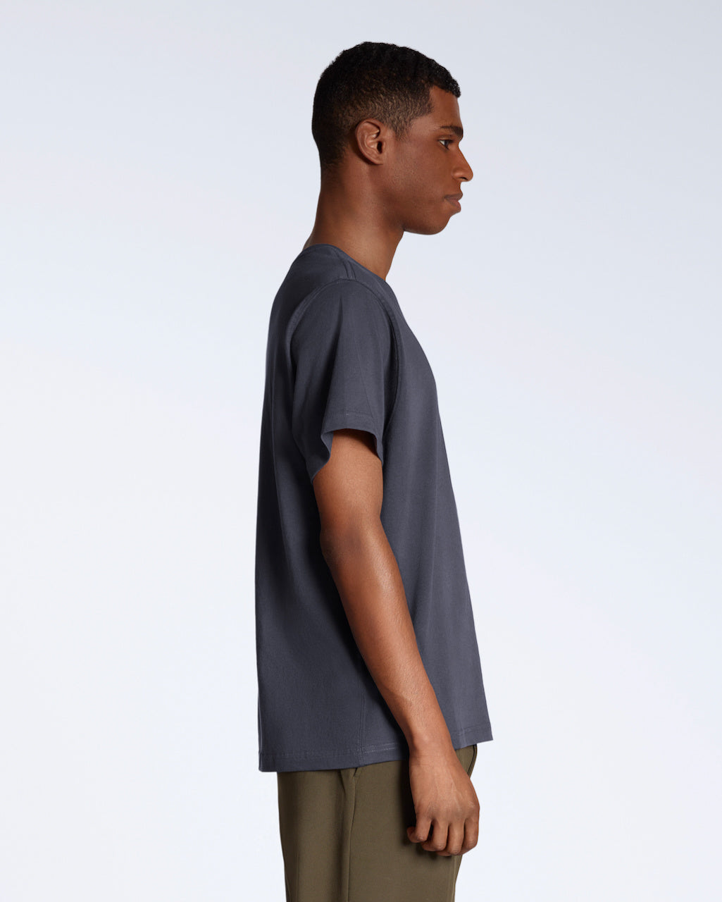 A man facing side on, modelling a plain dark grey, short sleeve organic cotton t shirt.