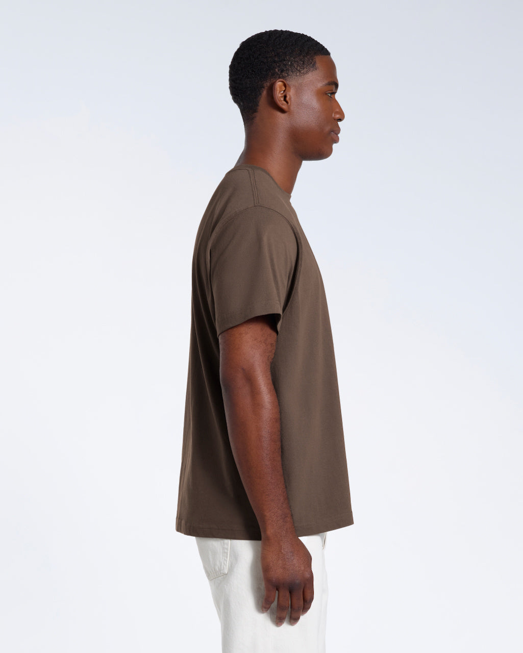 A man facing side on, modelling a plain dark khaki short sleeve organic cotton t shirt.
