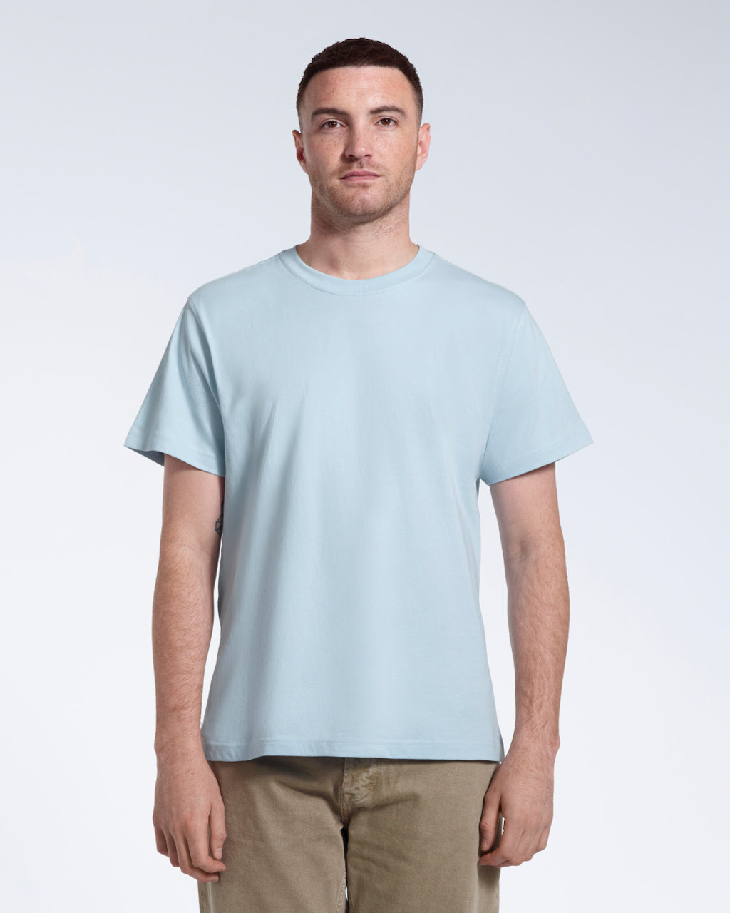 A man facing front on looking into the camera, modelling a plain light blue short sleeve organic cotton t shirt.