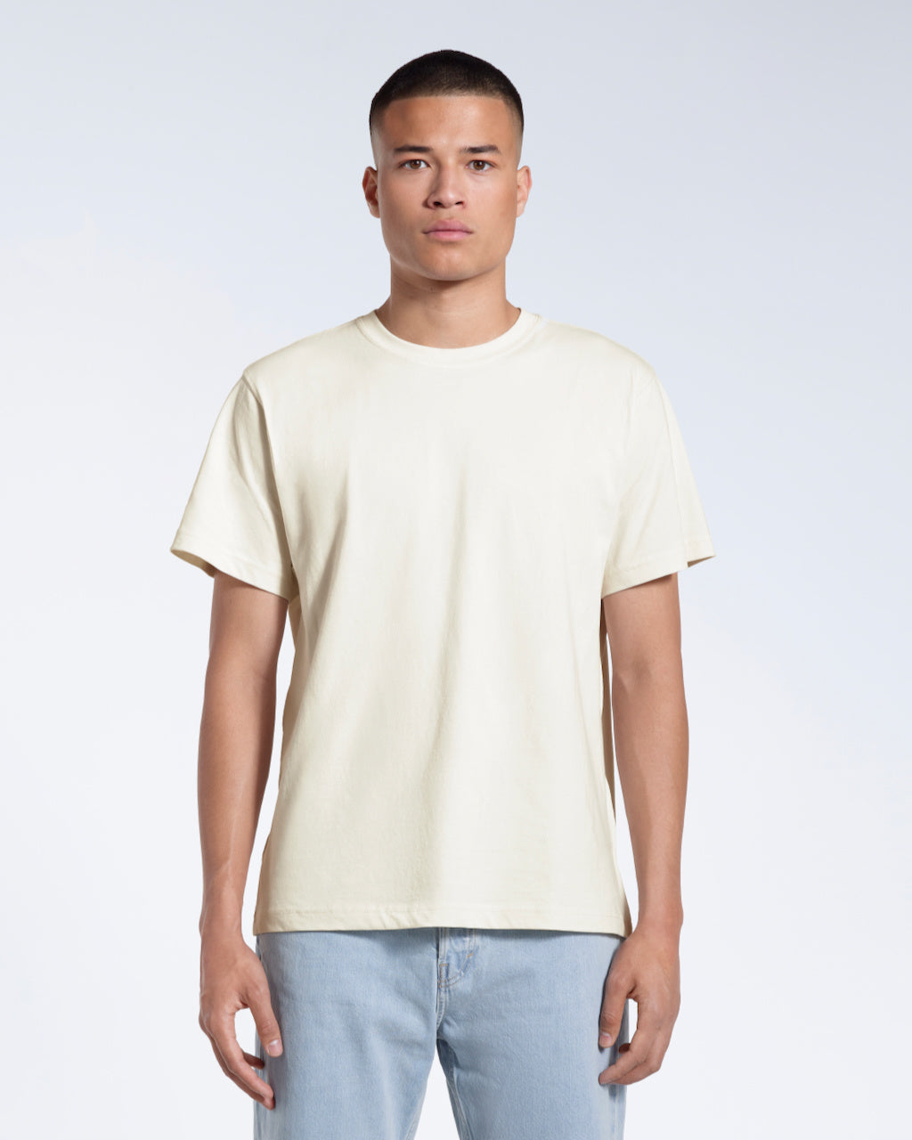 A man facing front on looking into the camera, modelling a plain ecru short sleeve organic cotton t shirt.