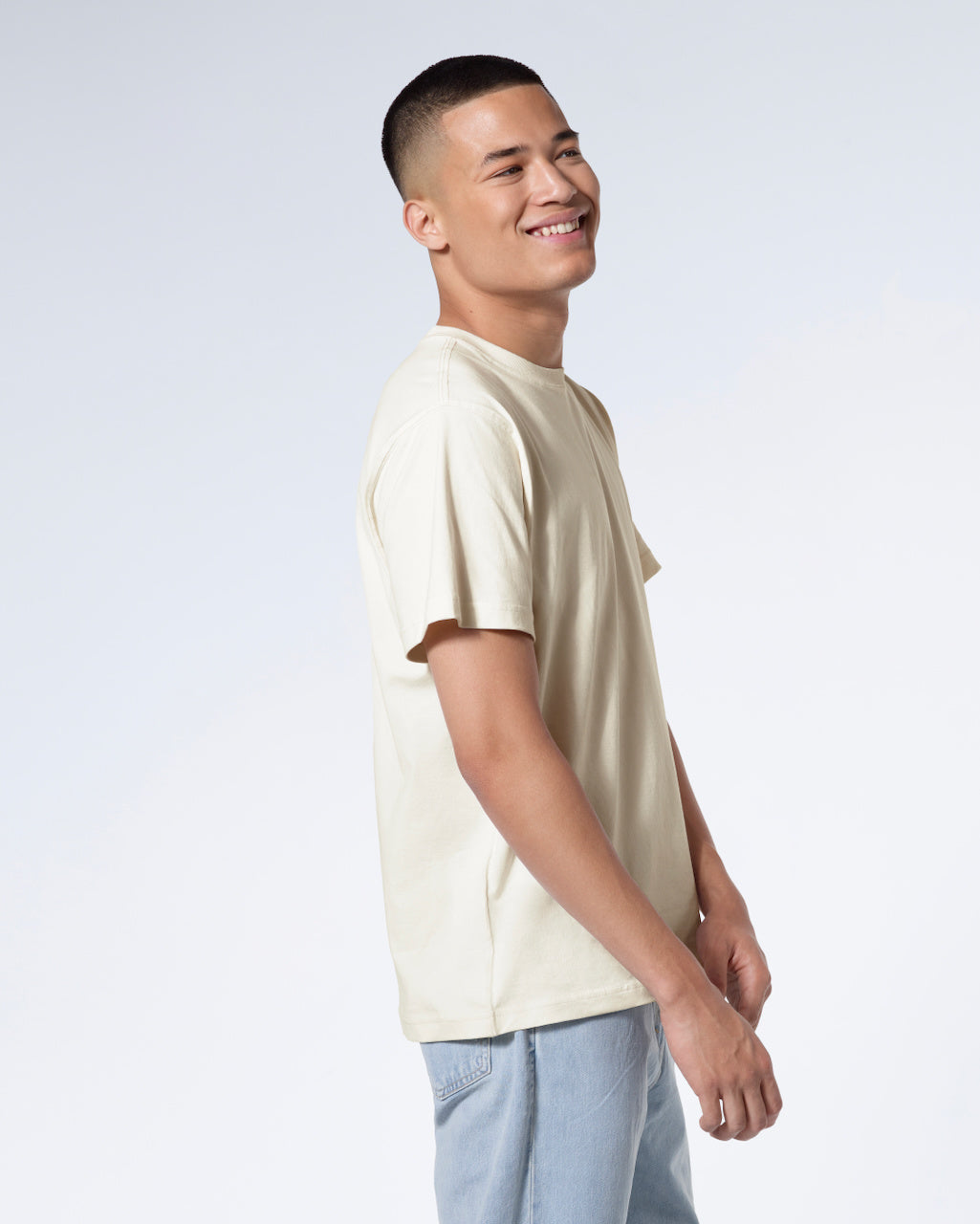 A man facing side on smiling, modelling a plain ecru short sleeve organic cotton t shirt.