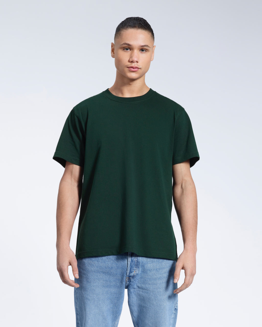 A man facing front on looking into the camera, modelling a plain green short sleeve organic cotton t shirt.