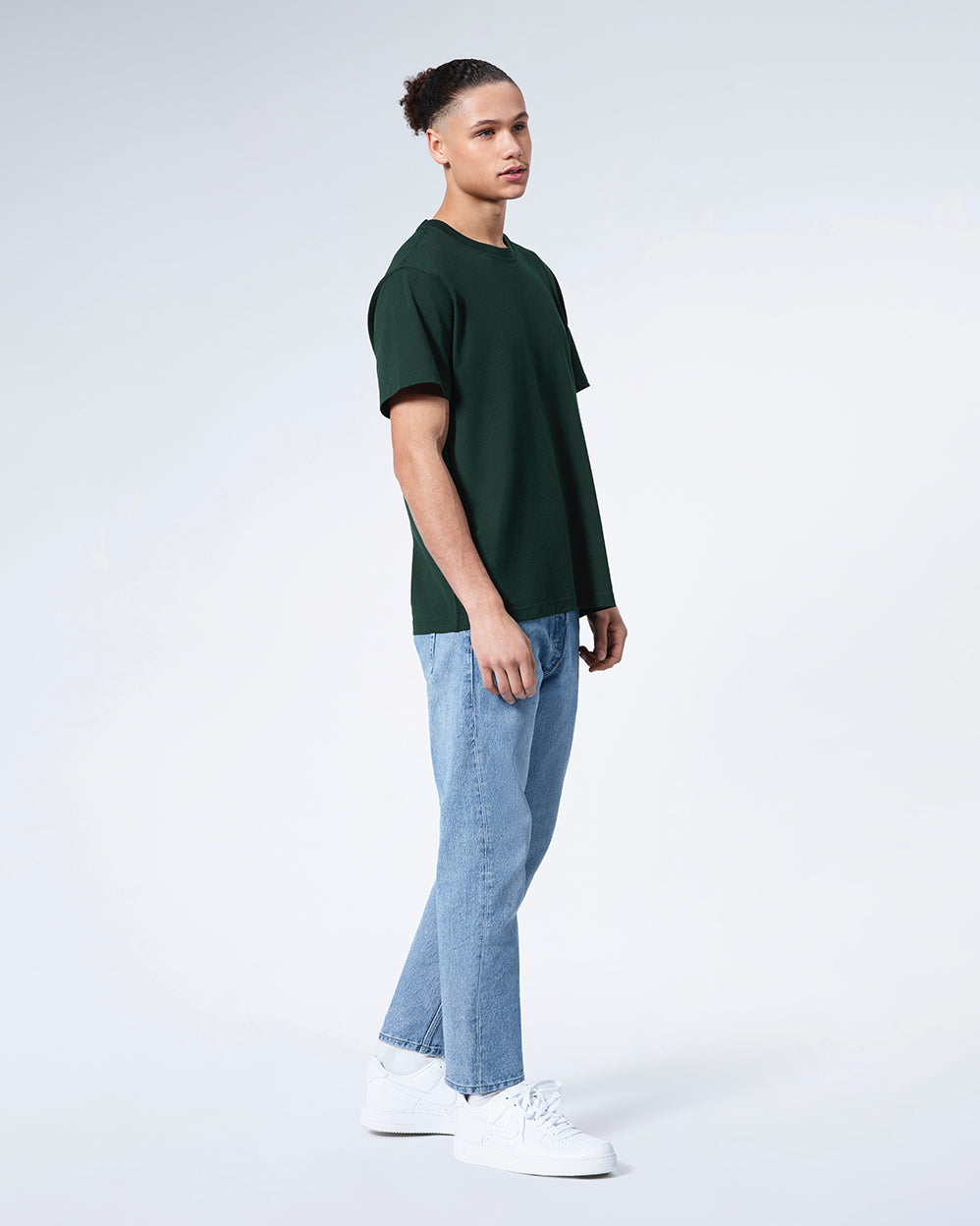 A full body photo of a man with his arms by his sides, modelling a plain green short sleeve organic cotton t shirt.