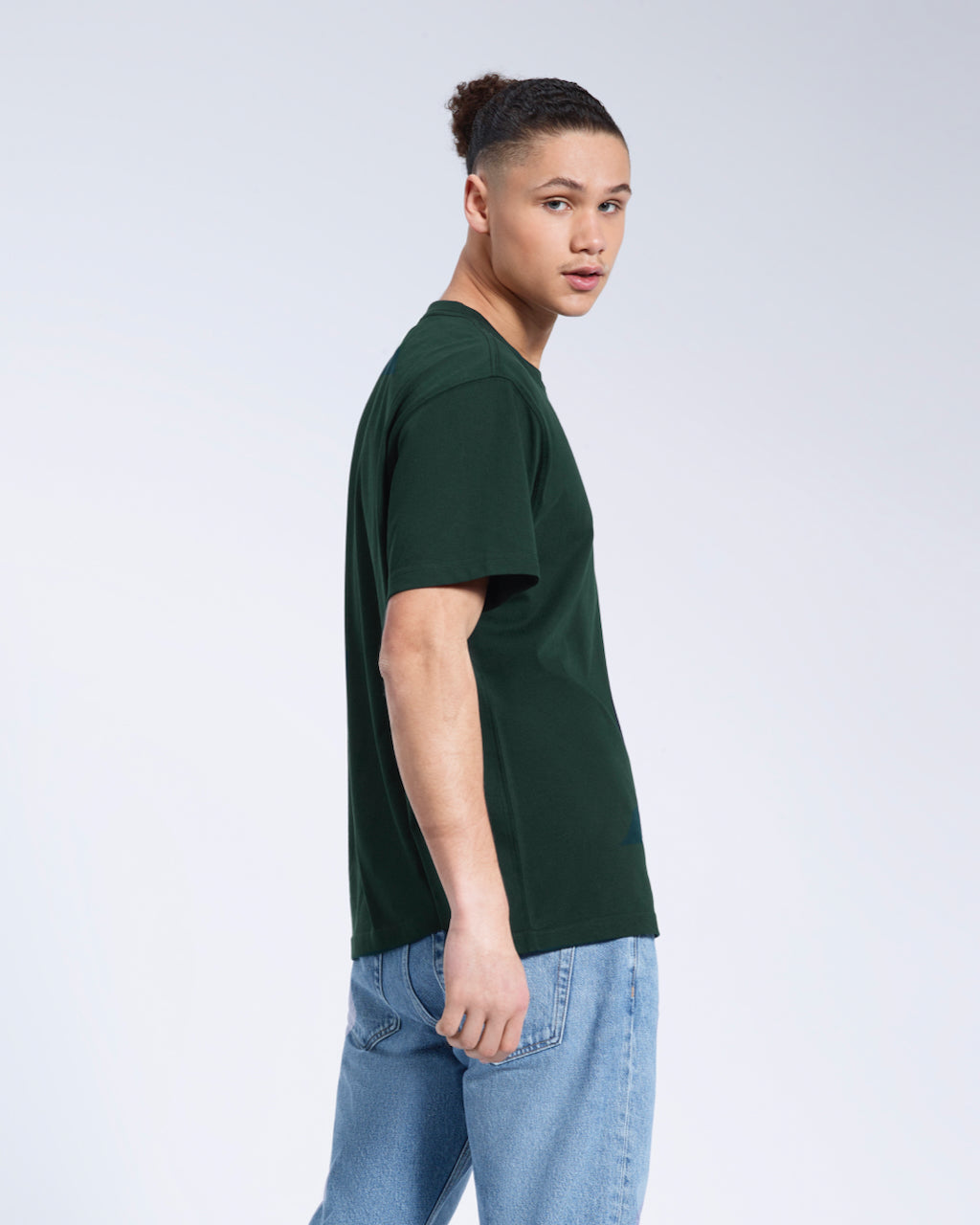 A man looking back towards the camera, modelling a plain green short sleeve organic cotton t shirt.