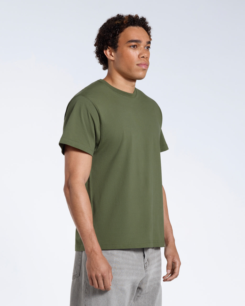 A man at an angle with his arms by his sides, modelling a plain khaki green short sleeve organic cotton t shirt.
