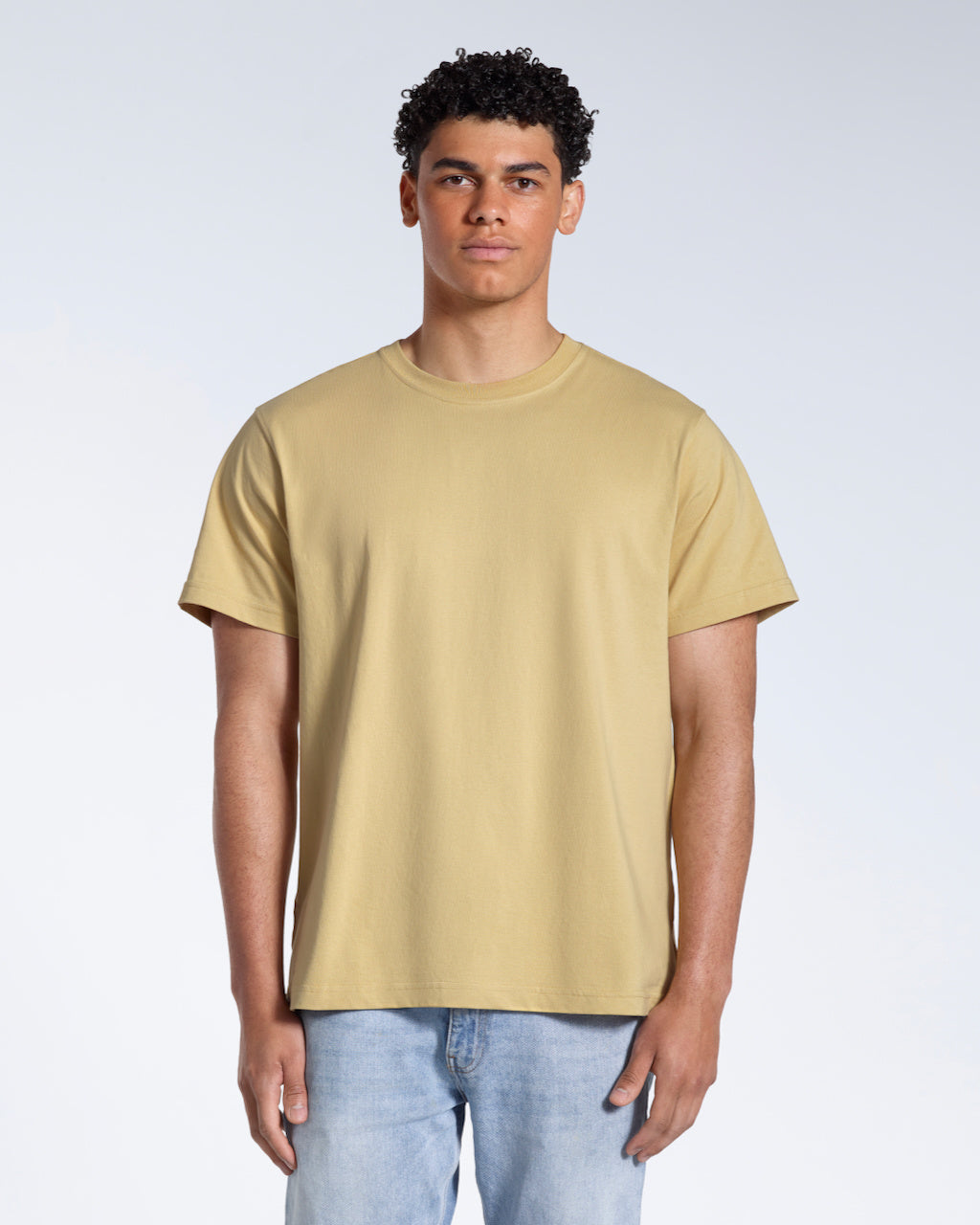 A man facing front on looking into the camera, modelling a plain light khaki short sleeve organic cotton t shirt.