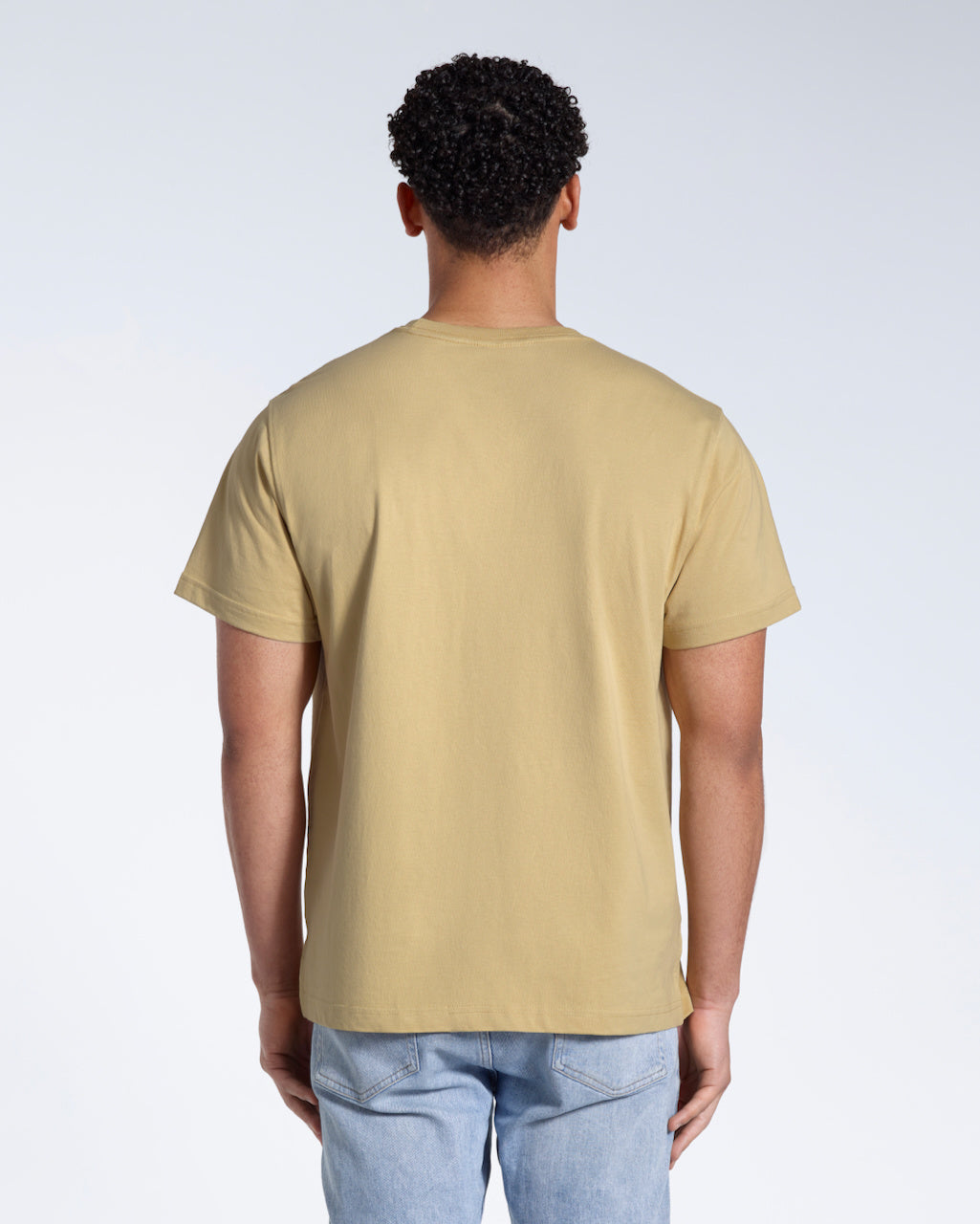 A man facing away from the camera, modelling a plain light khaki short sleeve organic cotton t shirt.