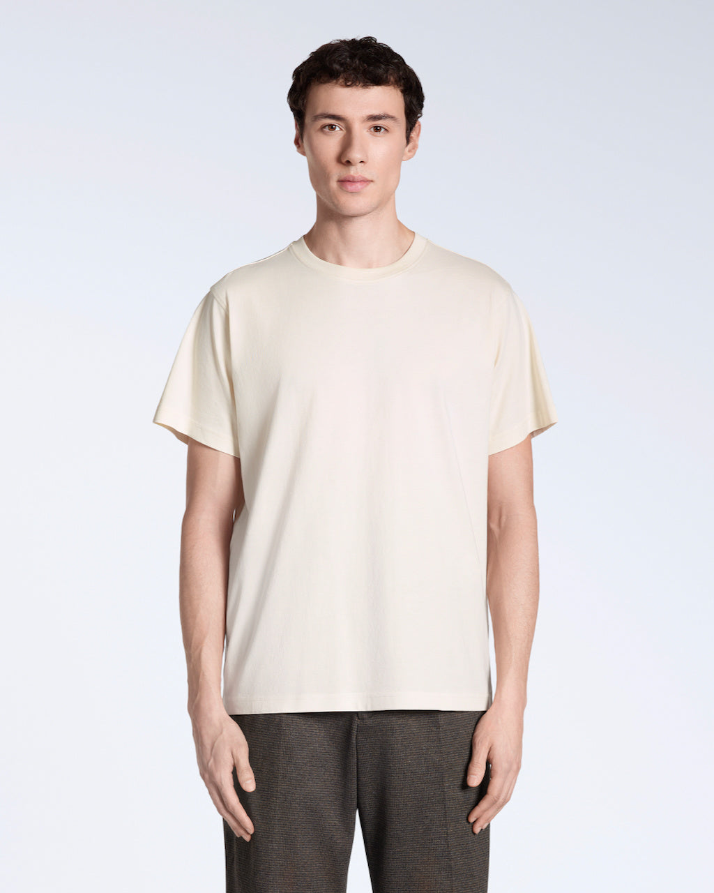 A man facing front on, modelling a plain natural coloured, short sleeve organic cotton t shirt.