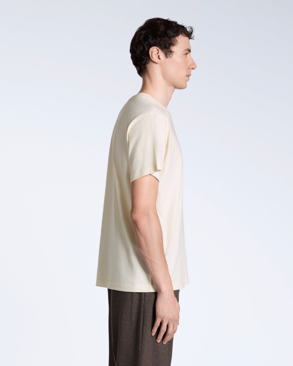 A man facing side on, modelling a plain natural coloured, short sleeve organic cotton t shirt.