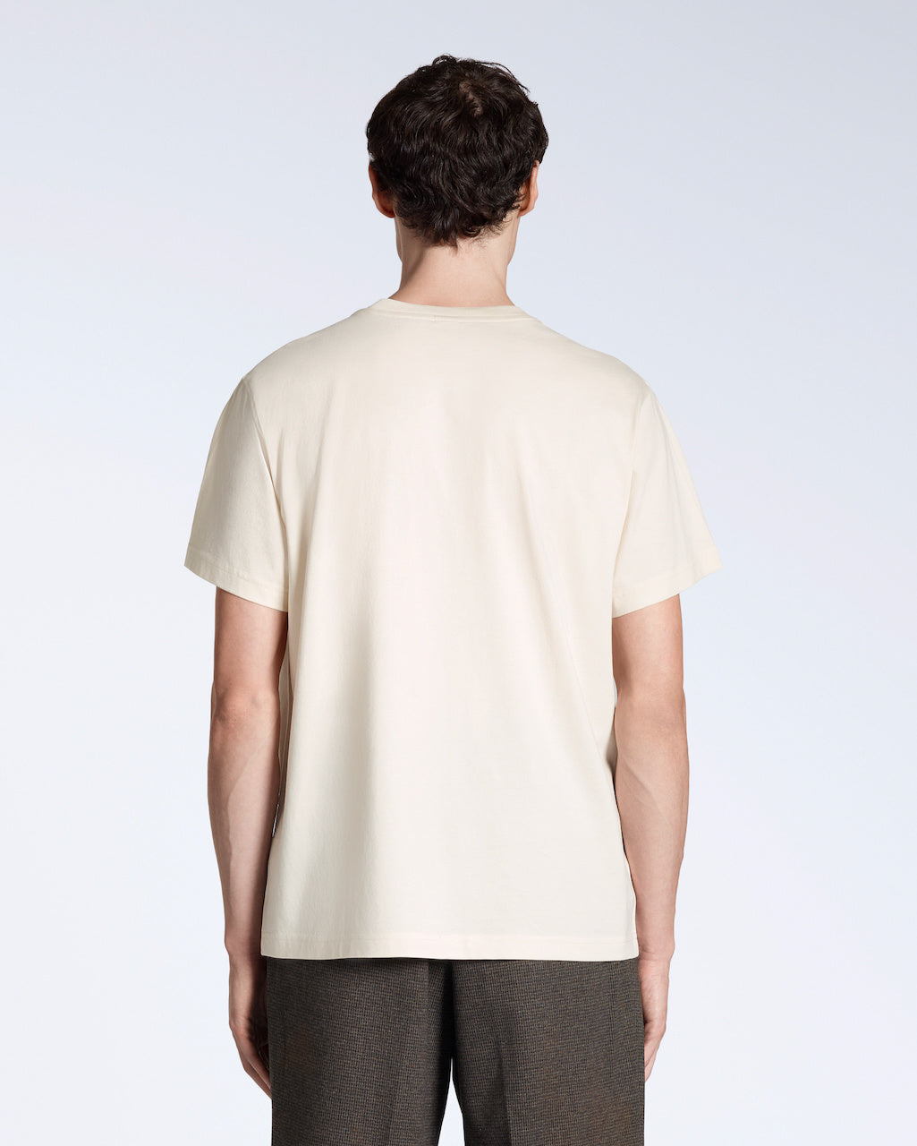 A man facing away from the camera, modelling a plain natural coloured, short sleeve organic cotton t shirt.