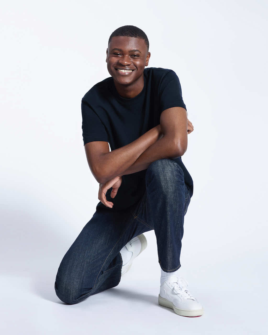 A man kneeling down smiling, modelling a plain navy short sleeve organic cotton t shirt.