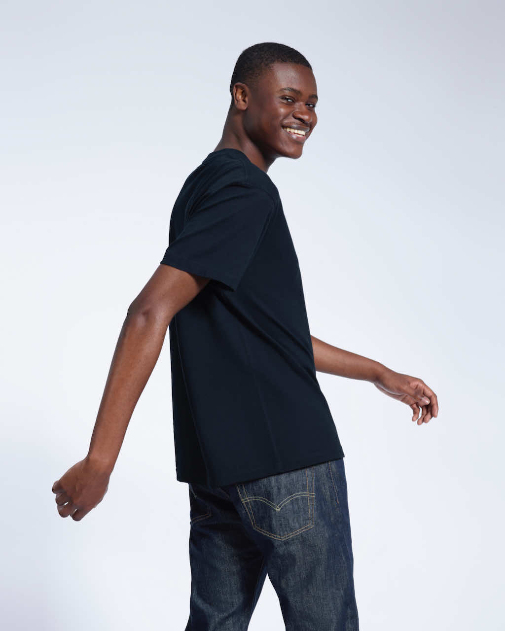 A man looking back smiling, modelling a plain navy short sleeve organic cotton t shirt.