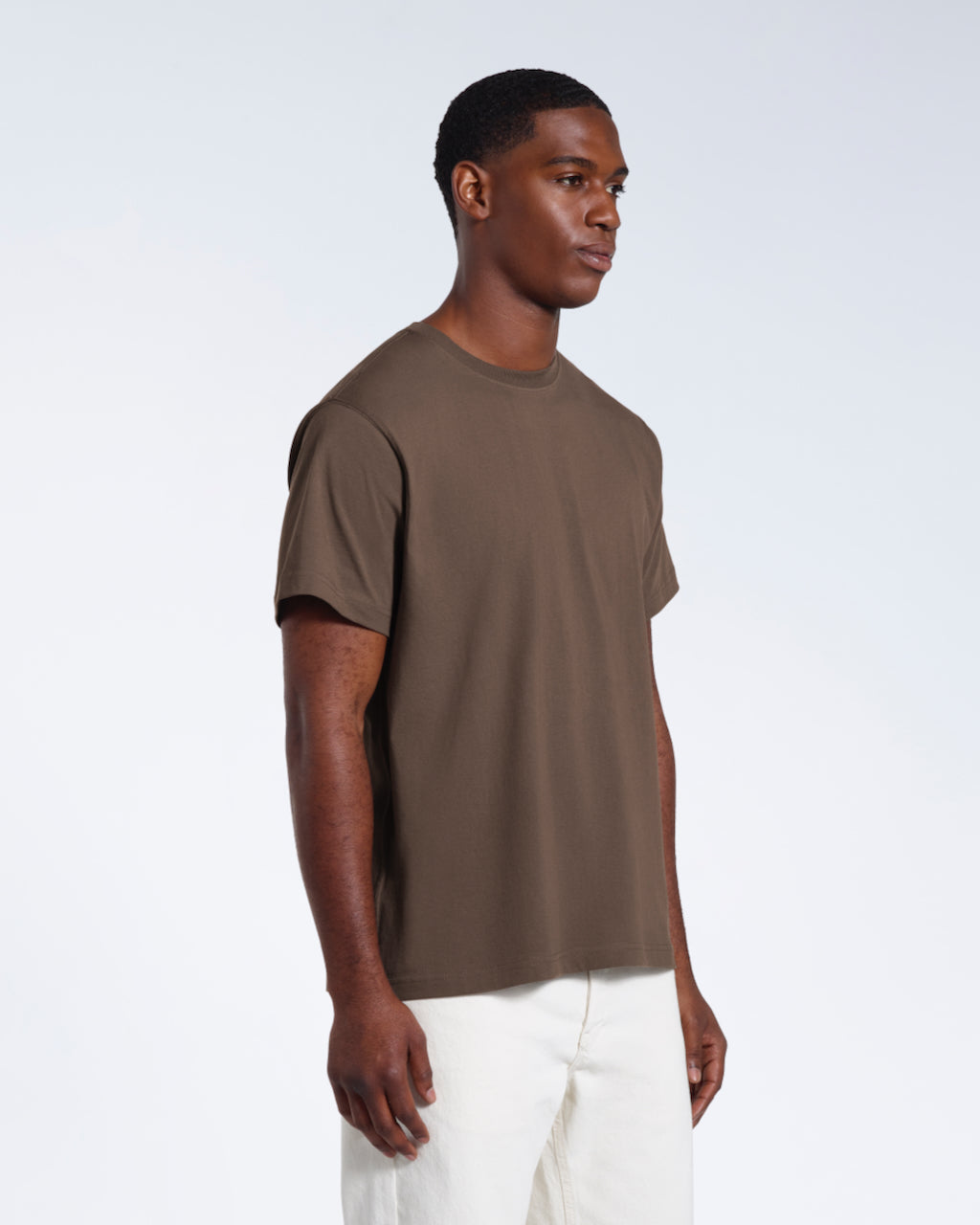 A man at an angle with his arms by his sides, modelling a plain dark khaki short sleeve organic cotton t shirt.