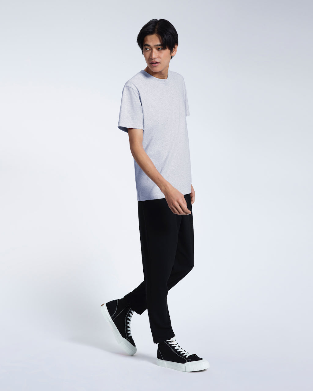 A full body photo of a man walking, modelling a grey short sleeve organic cotton t shirt.