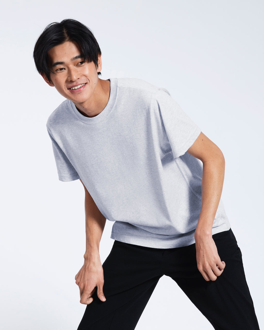 A man leaning over slightly, smiling, modelling a plain short sleeve grey organic cotton t shirt.