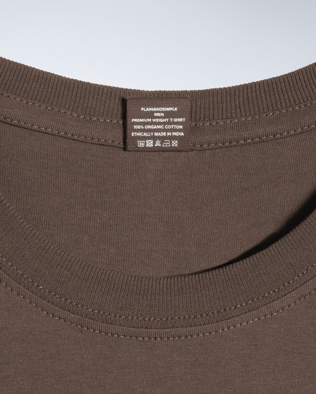 A close up of a neck label in a men's dark khaki short sleeve crew neck organic cotton t shirt.