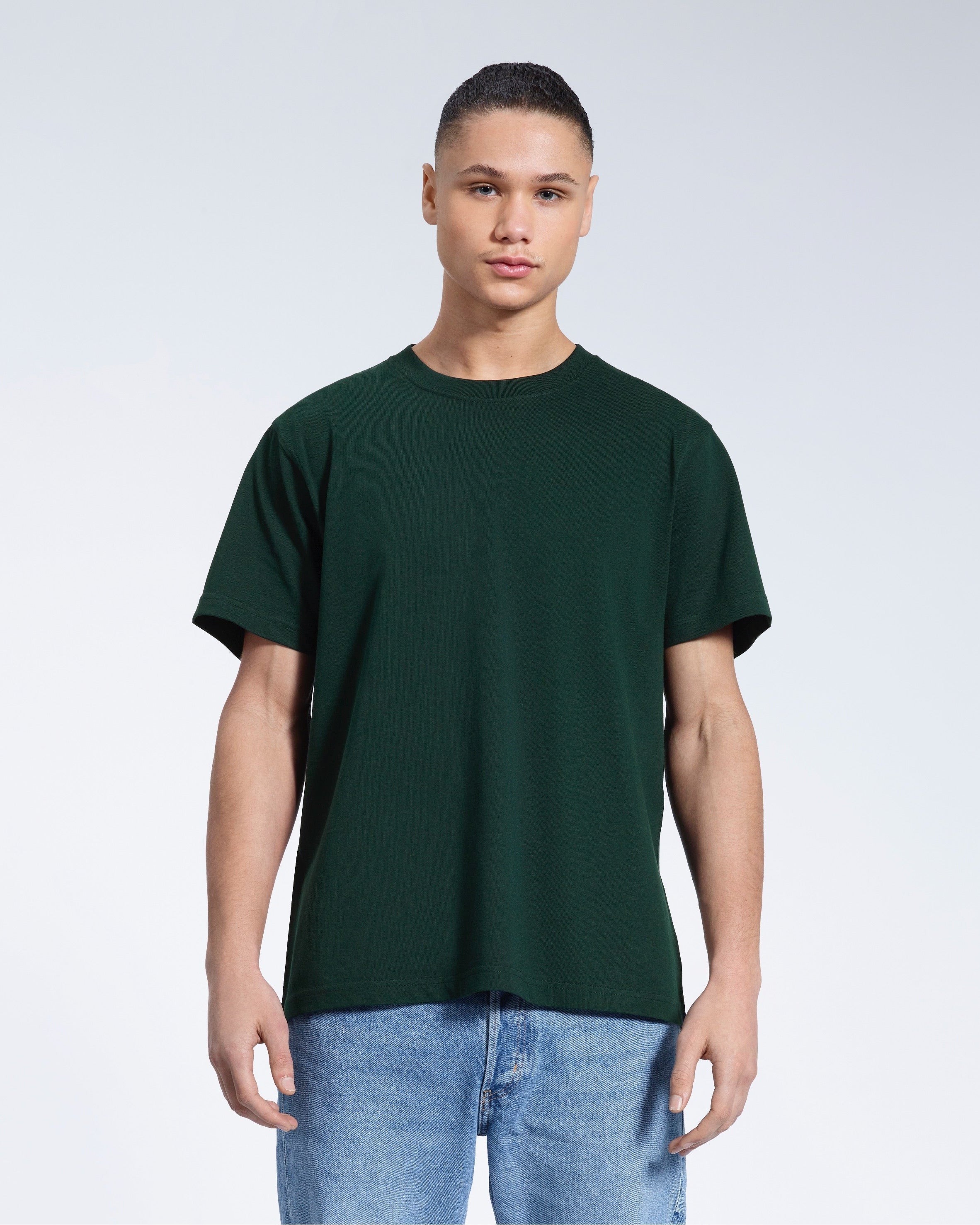 A man facing front on looking into the camera, modelling a plain green short sleeve organic cotton t shirt.
