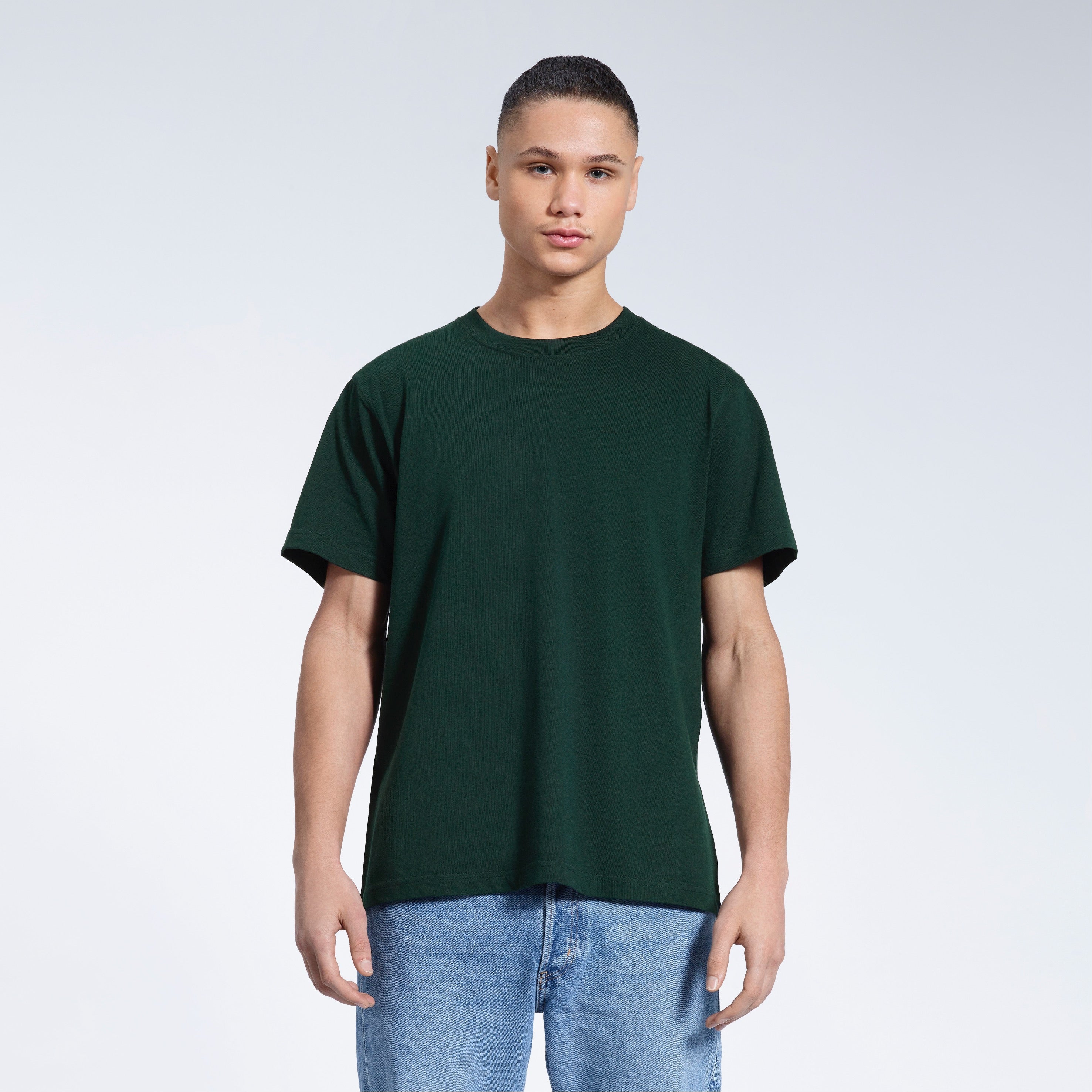 A man facing front on looking into the camera, modelling a plain green short sleeve organic cotton t shirt.