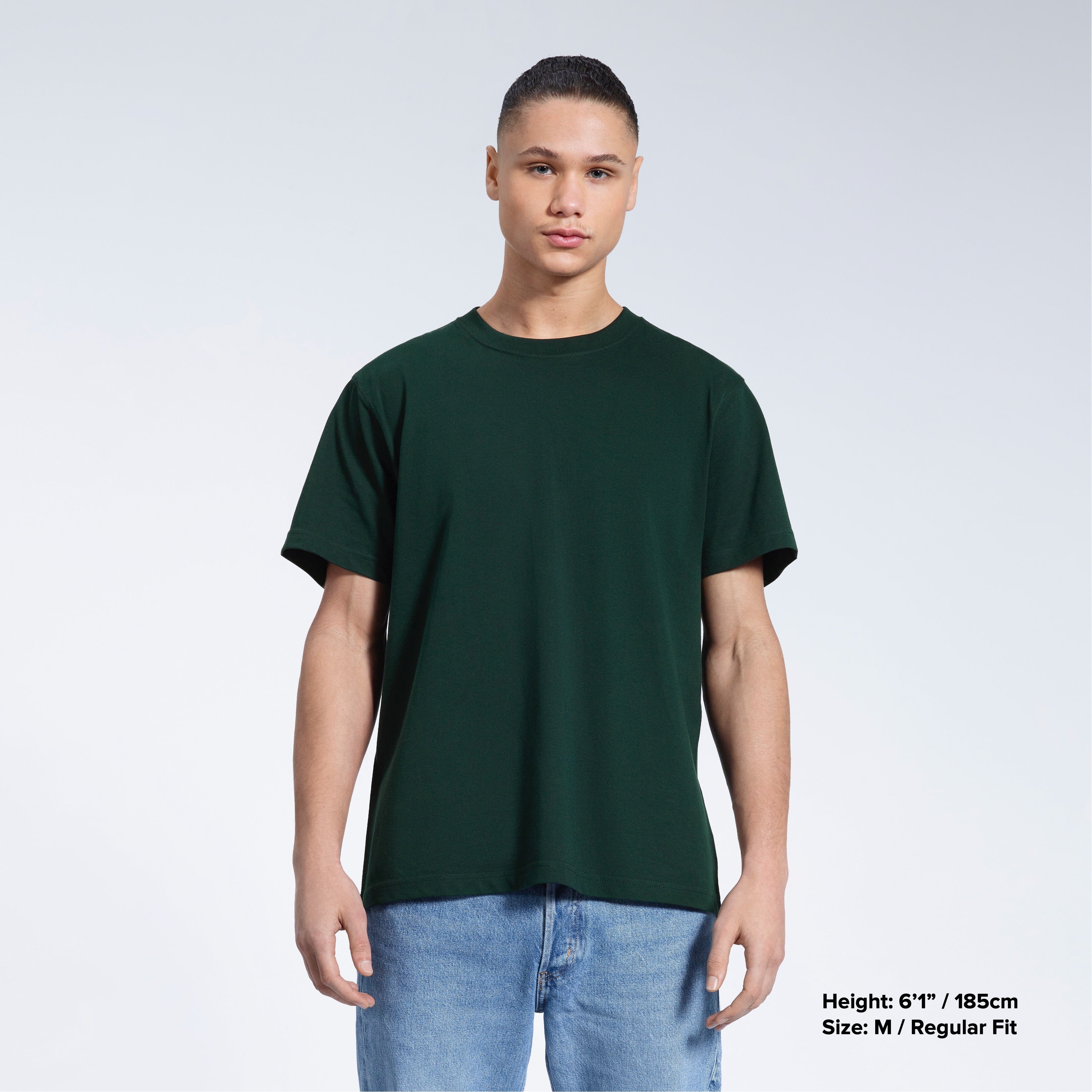 A man facing front on looking into the camera, modelling a plain green short sleeve organic cotton t shirt.
