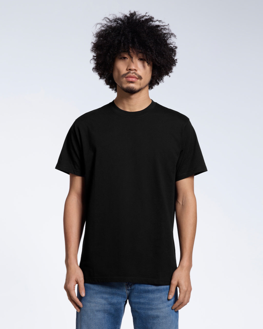 A man facing front on looking into the camera, modelling a plain black short sleeve organic cotton t shirt.