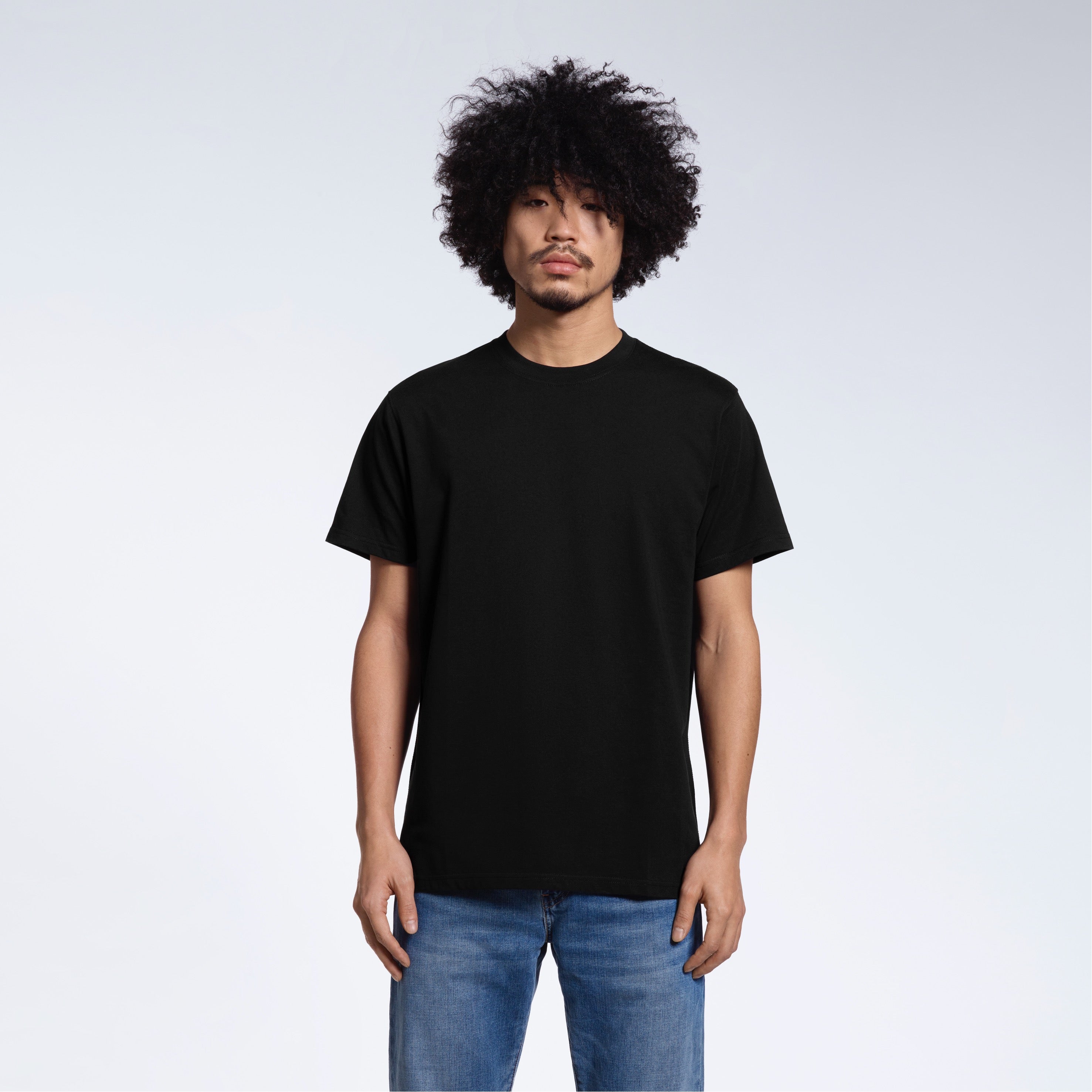 A man facing front on looking into the camera, modelling a plain black short sleeve organic cotton t shirt.