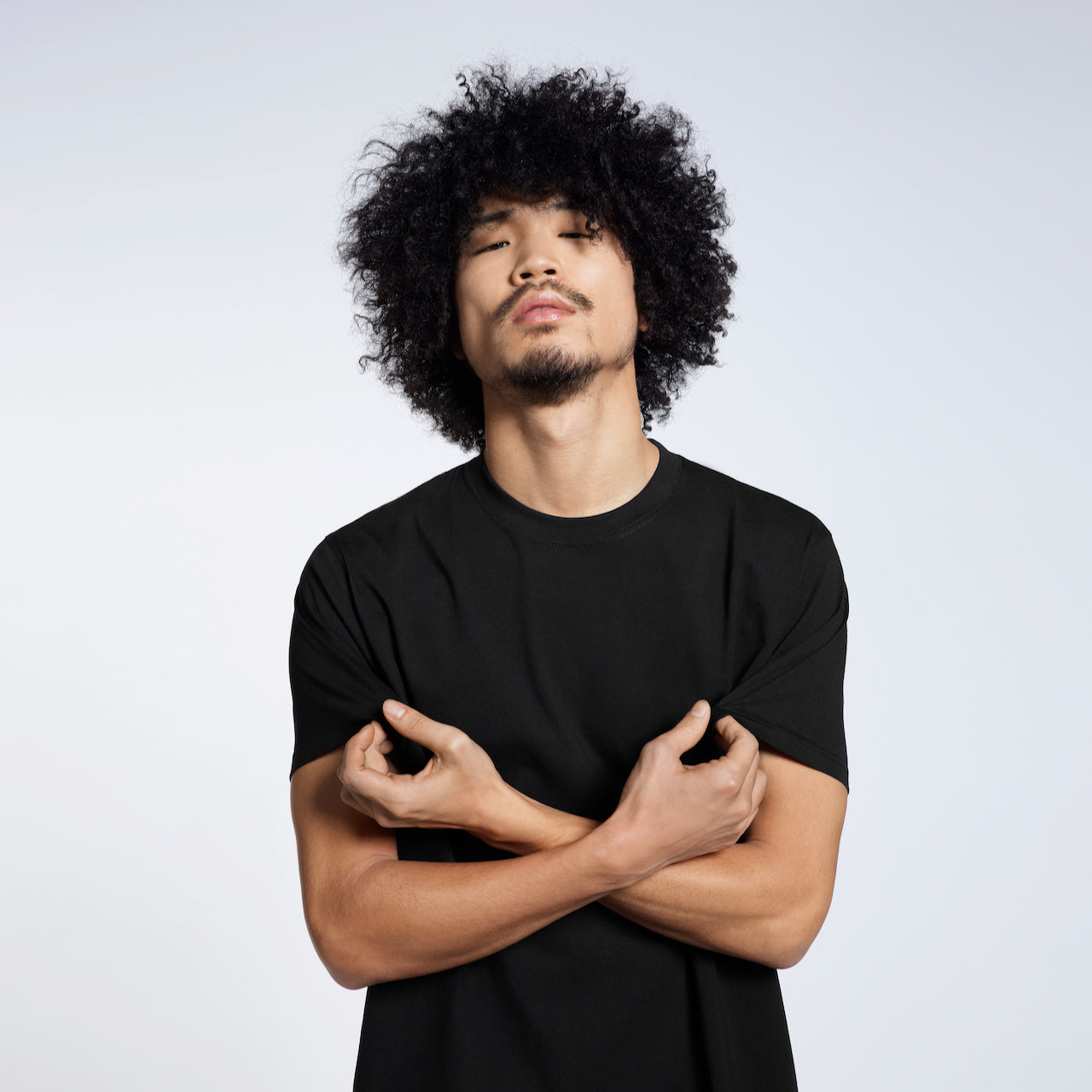 A man looking into the camera, touching his plain black short sleeve organic cotton t shirt.