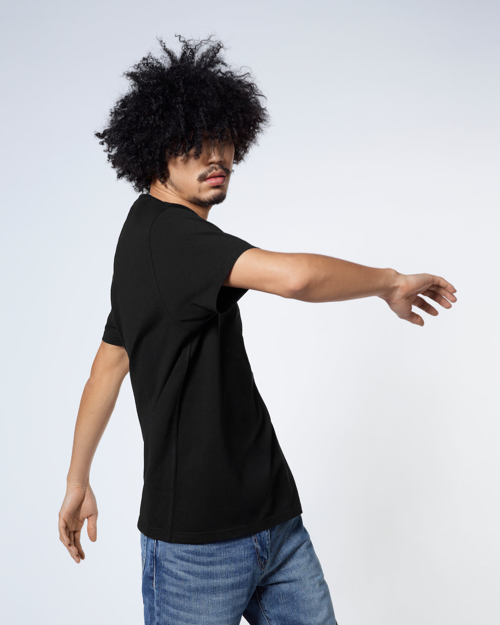 A man twisting his upper body, modelling a plain black short sleeve organic cotton t shirt.