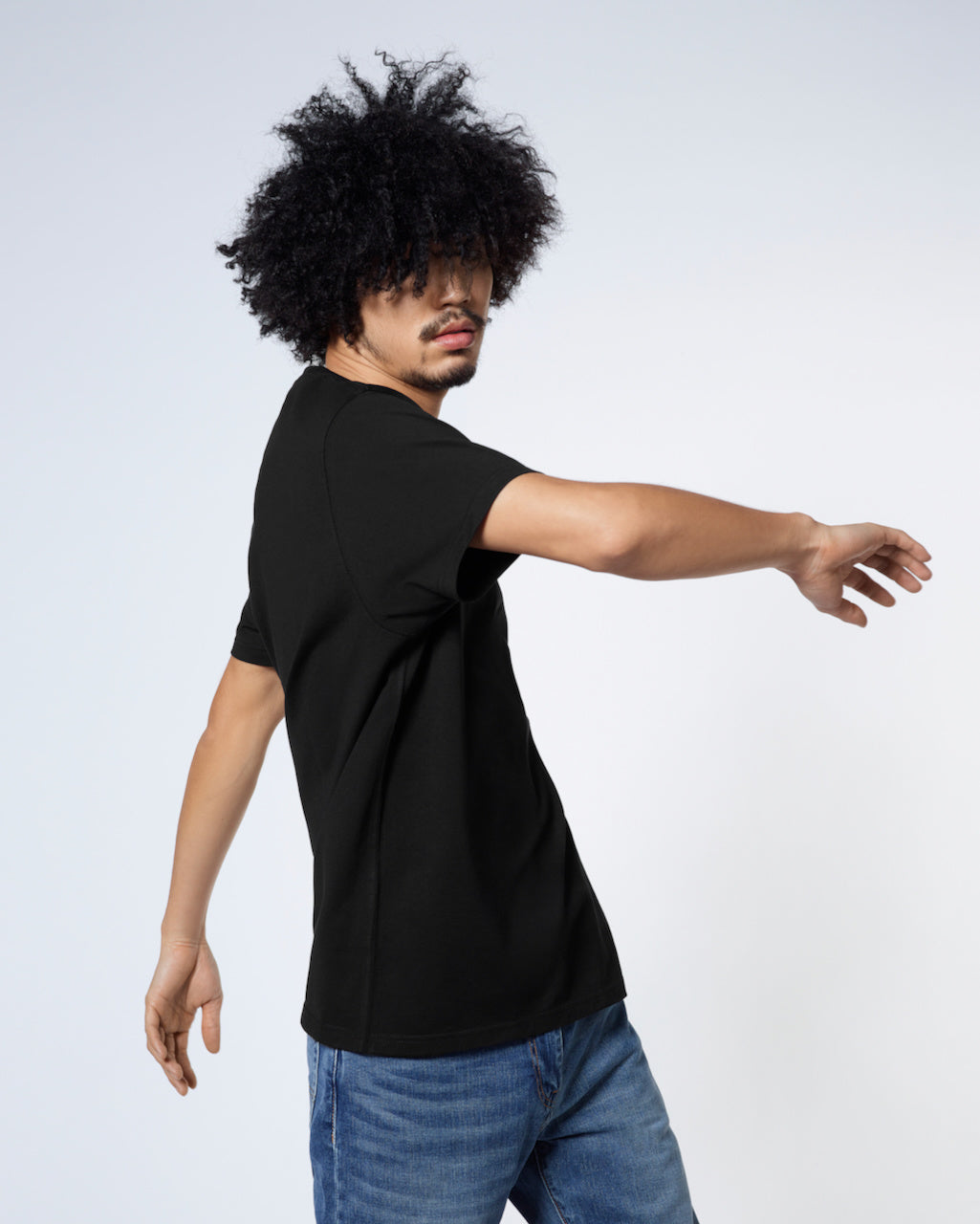 A man twisting his upper body, modelling a plain black short sleeve organic cotton t shirt.