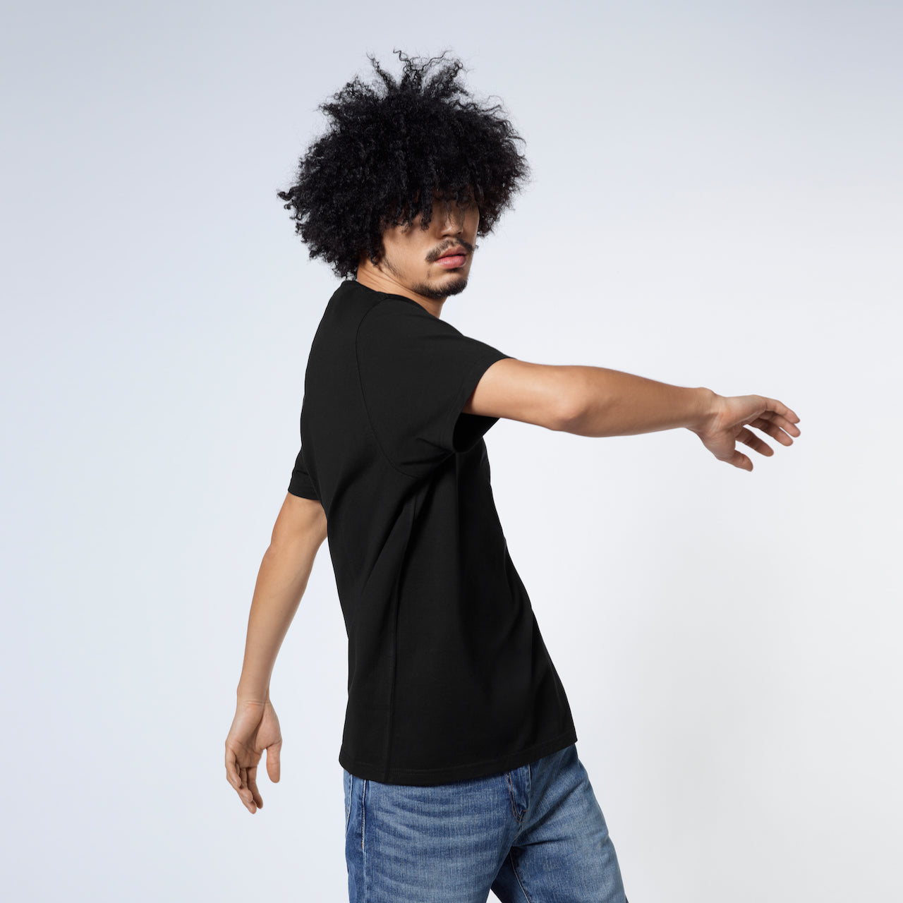 A man twisting his upper body, modelling a plain black short sleeve organic cotton t shirt.