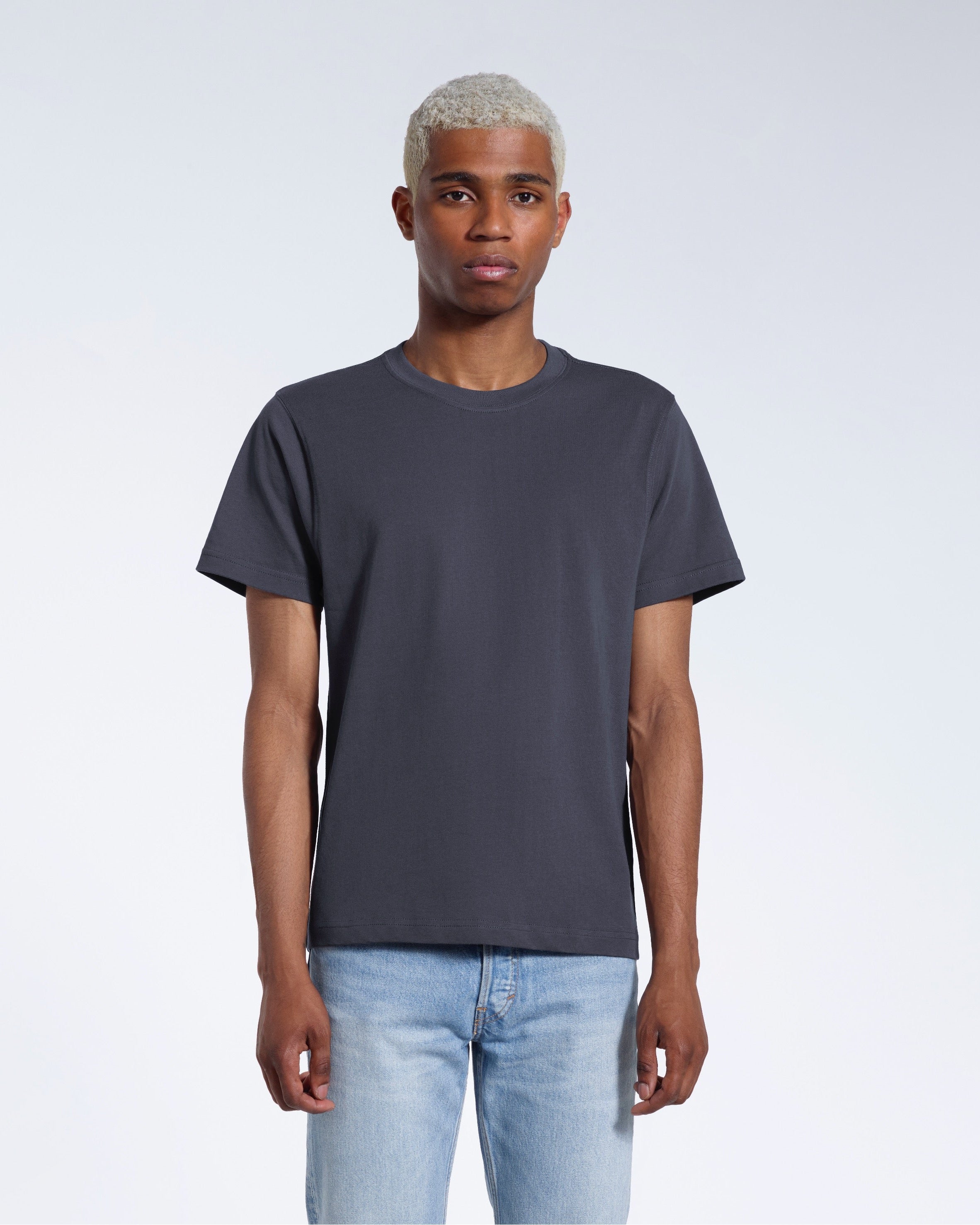 A man facing front on looking into the camera, modelling a plain dark grey short sleeve organic cotton t shirt.