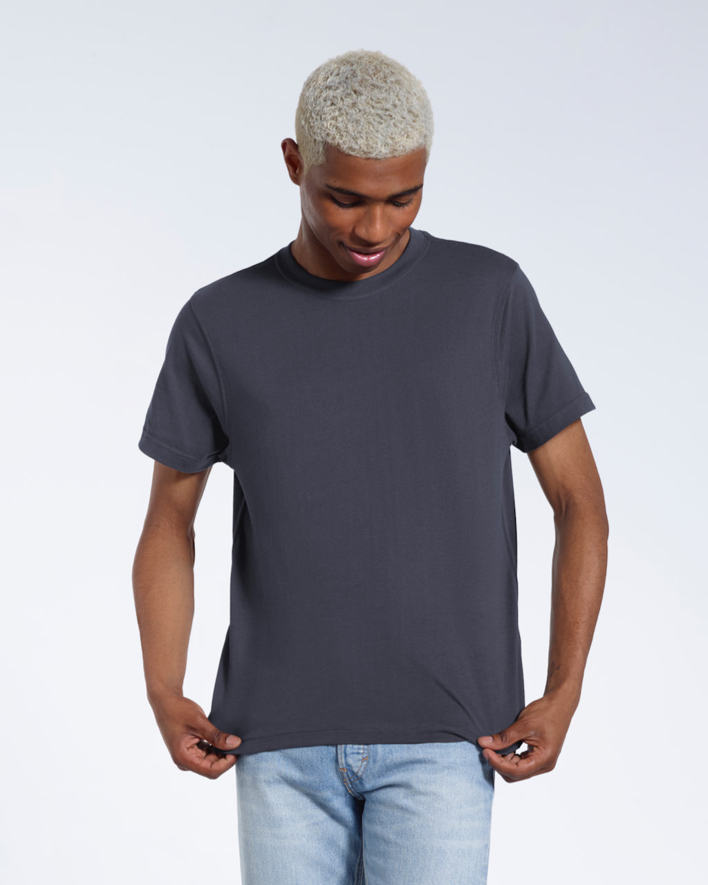 A man looking down and touching the bottom of his plain dark grey short sleeve organic cotton t shirt.