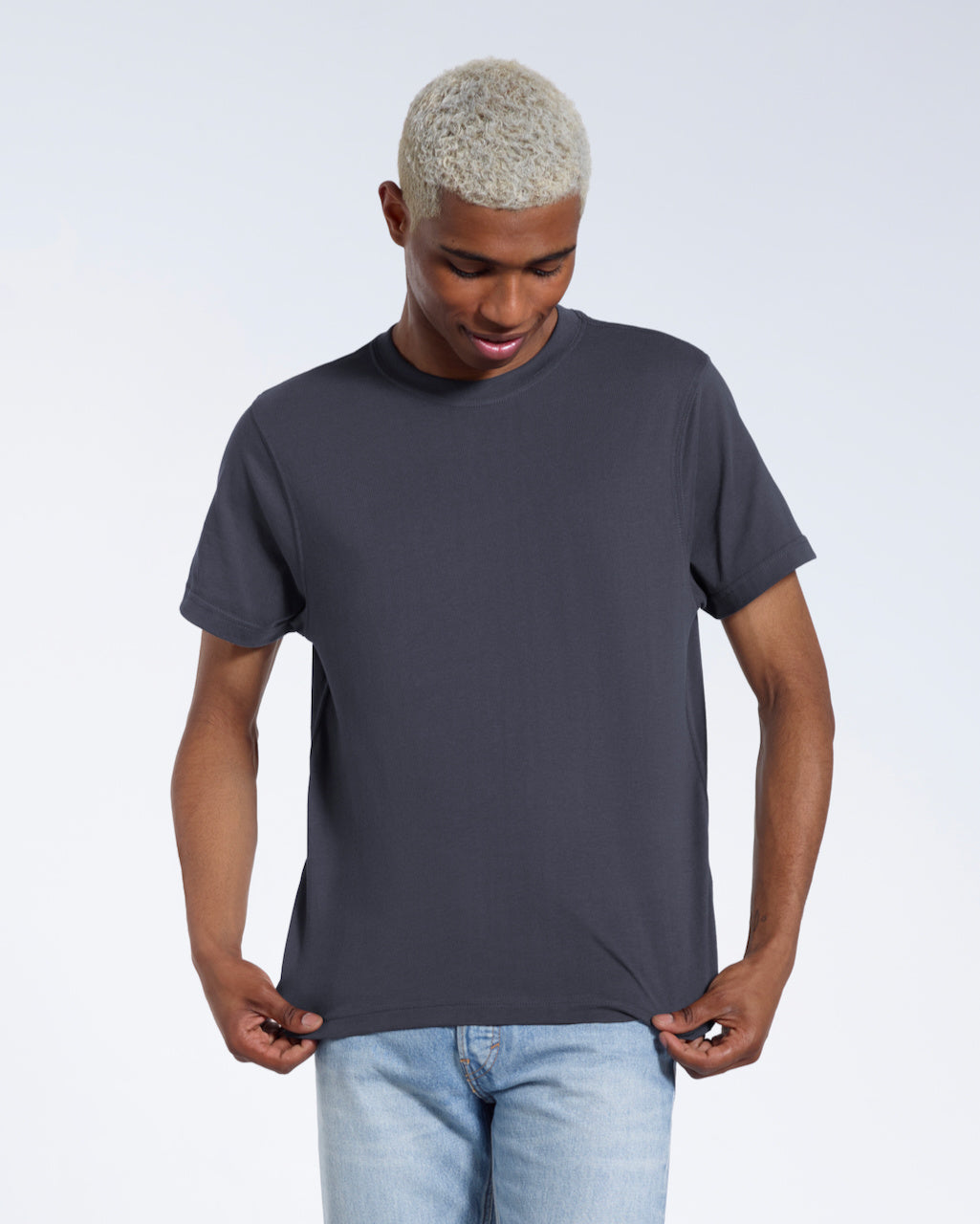 A man looking down and touching the bottom of his plain dark grey short sleeve organic cotton t shirt.
