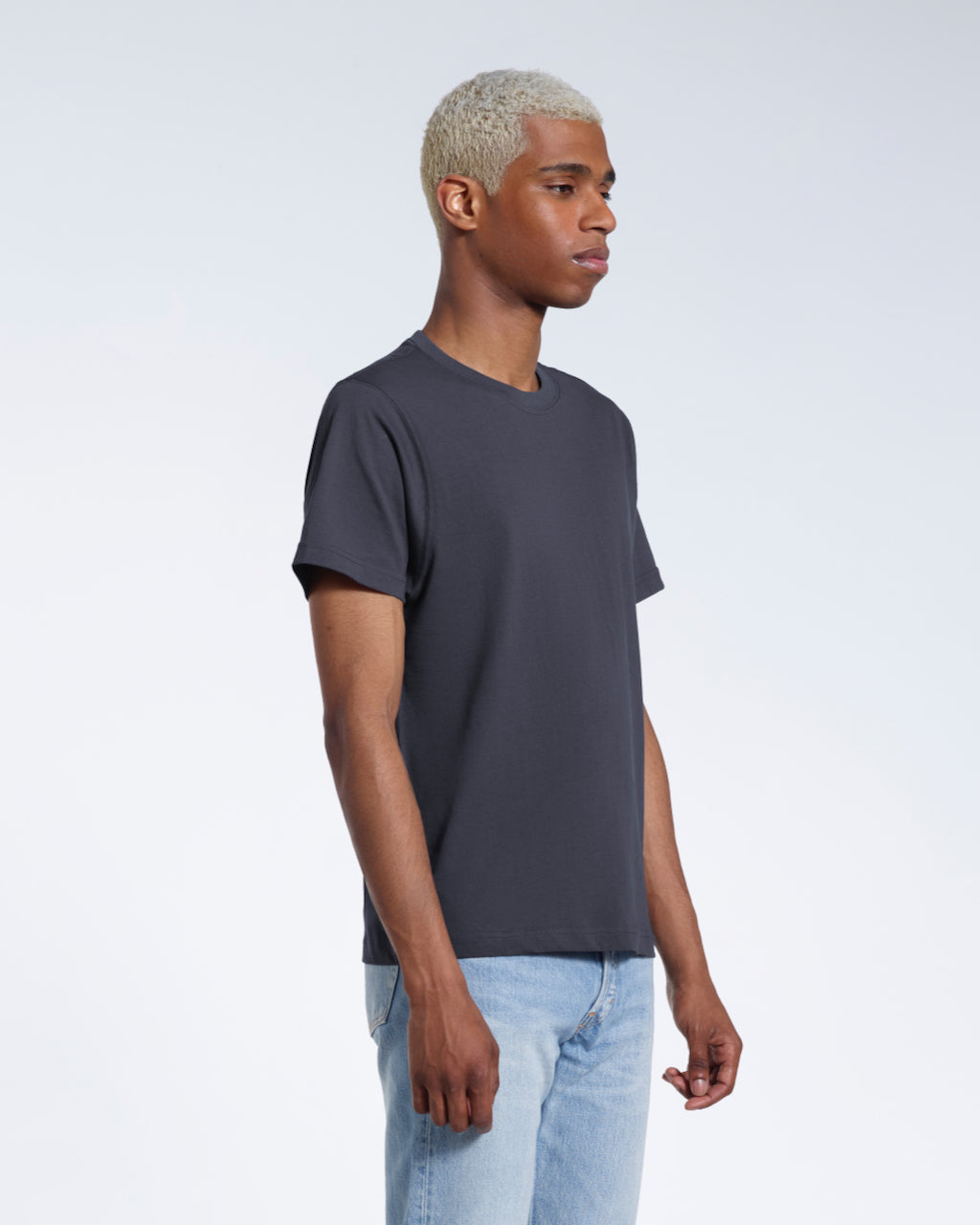 A man at an angle with his arms by his sides, modelling a plain dark grey short sleeve organic cotton t shirt.