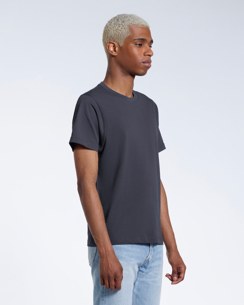 A man at an angle with his arms by his sides, modelling a plain dark grey short sleeve organic cotton t shirt.