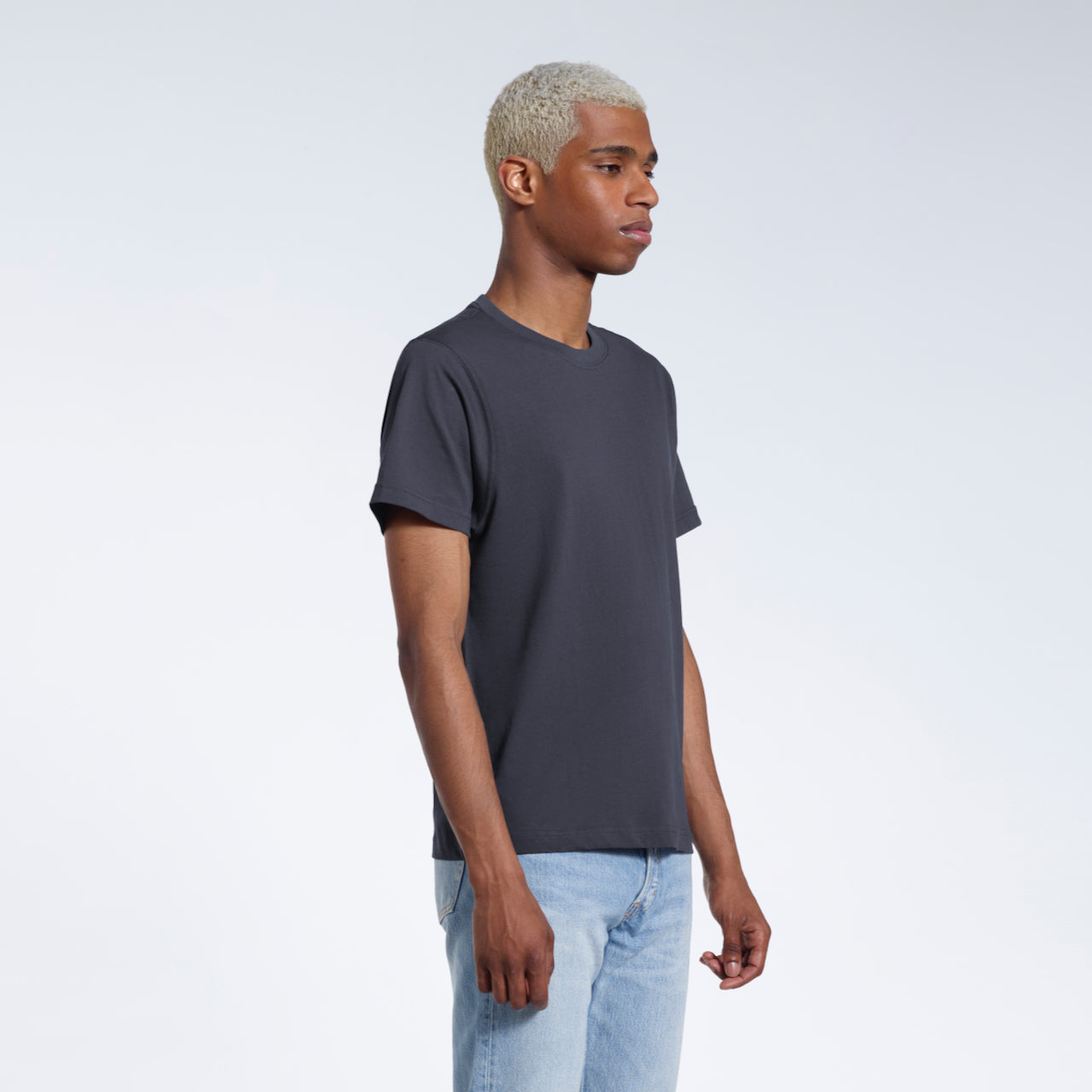 A man at an angle with his arms by his sides, modelling a plain dark grey short sleeve organic cotton t shirt.