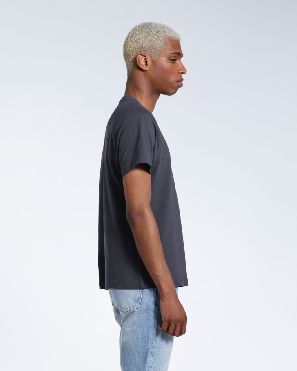 A man facing side on, modelling a plain dark grey short sleeve organic cotton t shirt.
