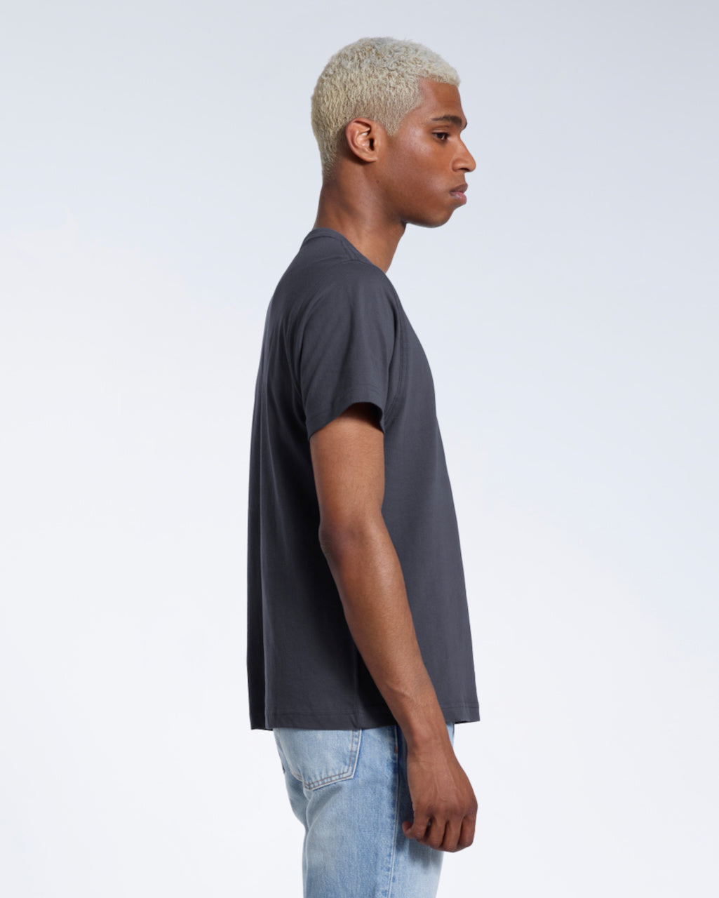 A man facing side on, modelling a plain dark grey short sleeve organic cotton t shirt.