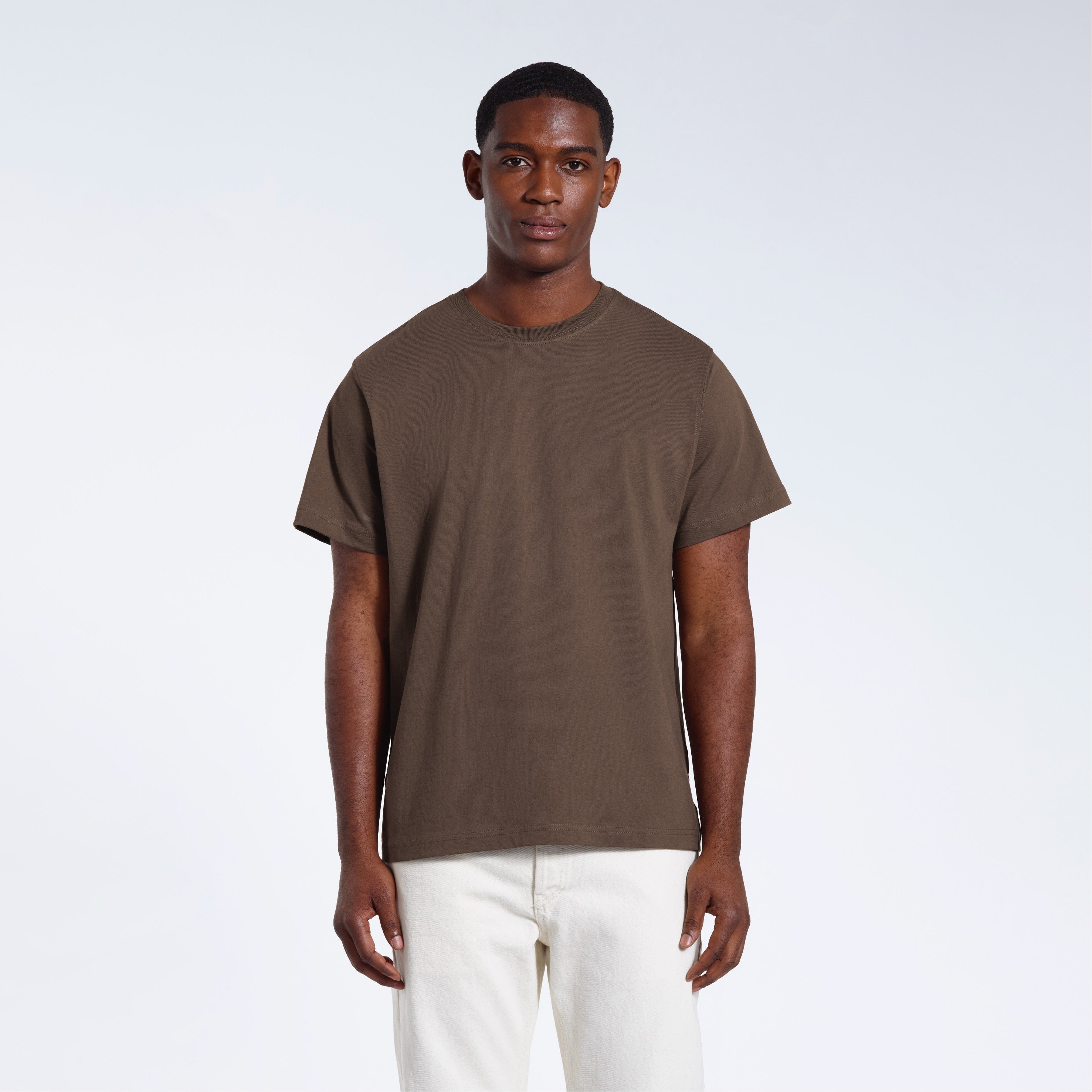 A man facing front on looking into the camera, modelling a plain dark khaki short sleeve organic cotton t shirt.
